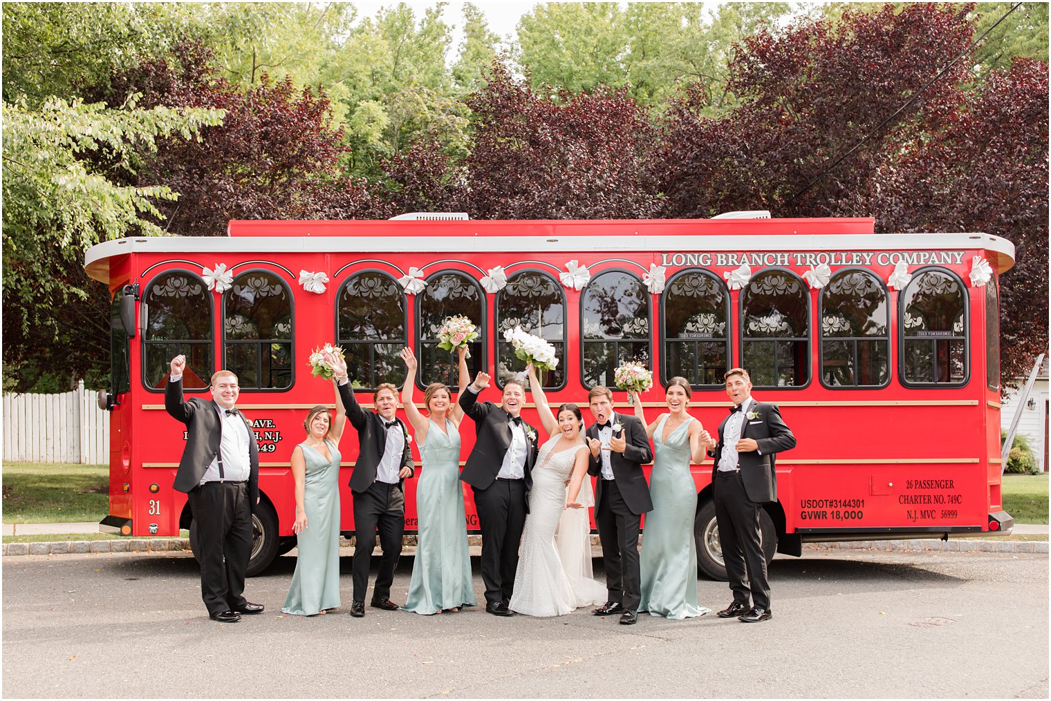 wedding party cheers with bride and groom by red Long Branch Trolley 