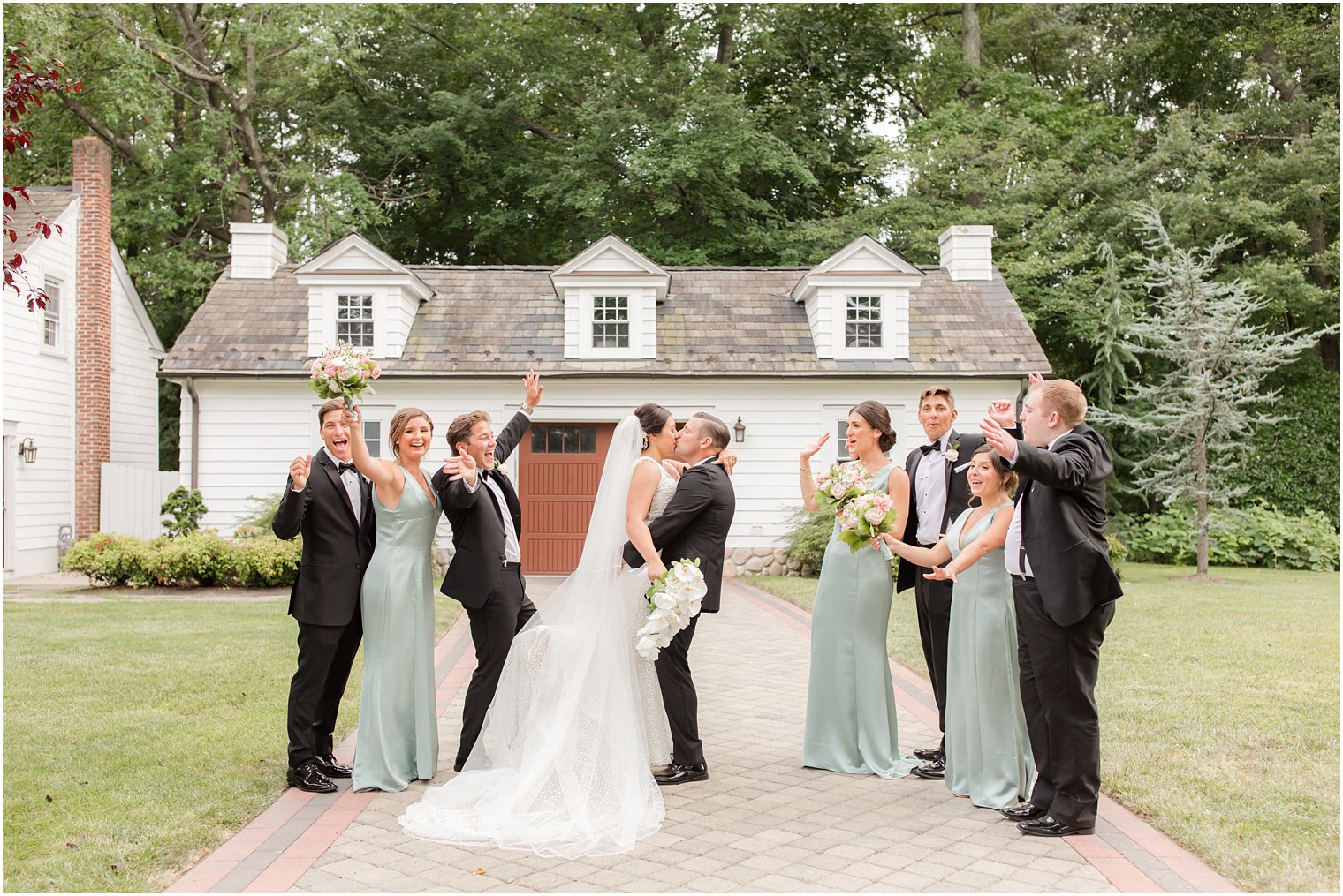 wedding party cheers while groom picks up bride kissing her
