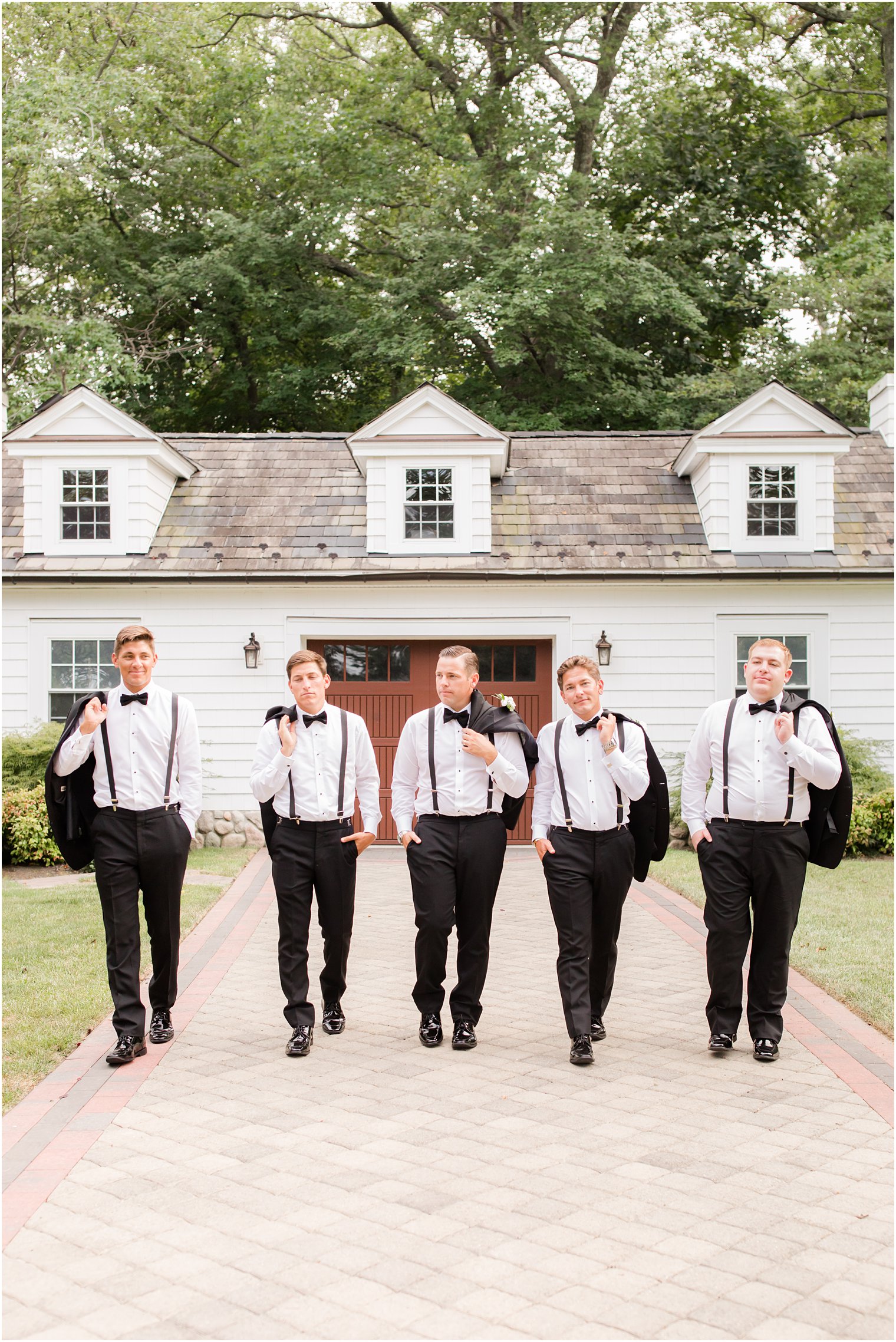 groom walks with groomsmen outside the English Manor with jackets over their shoulders