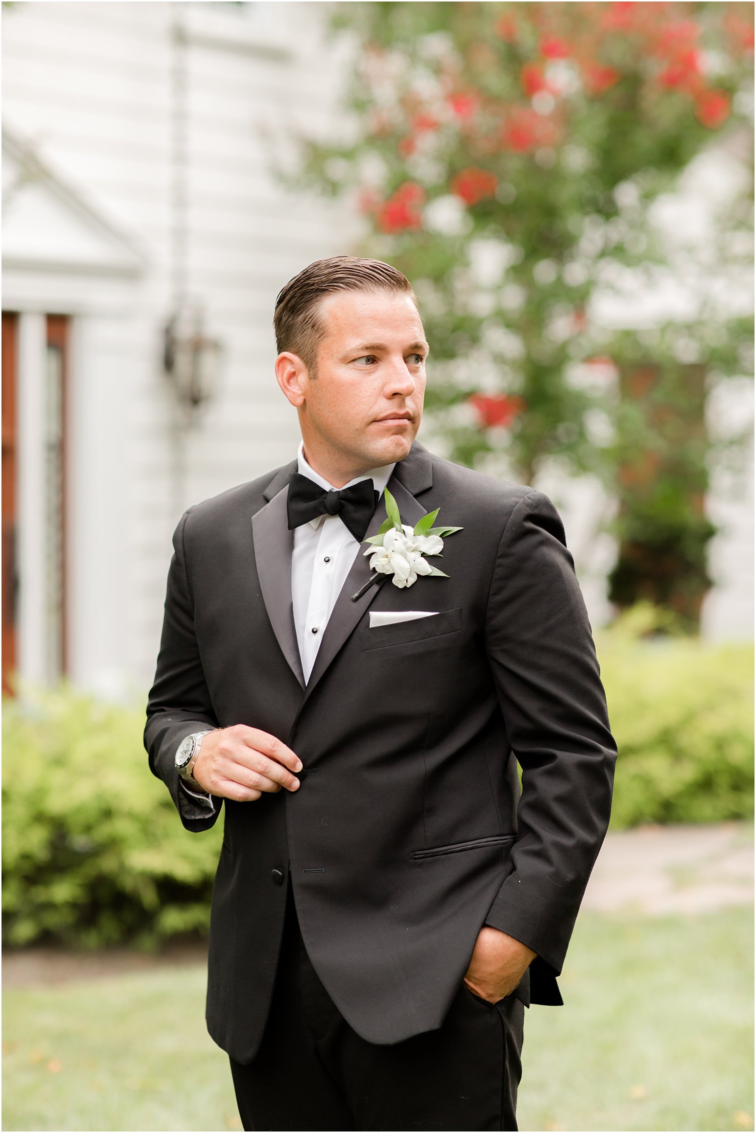 groom in classic black tux poses on lawn in Ocean Township NJ