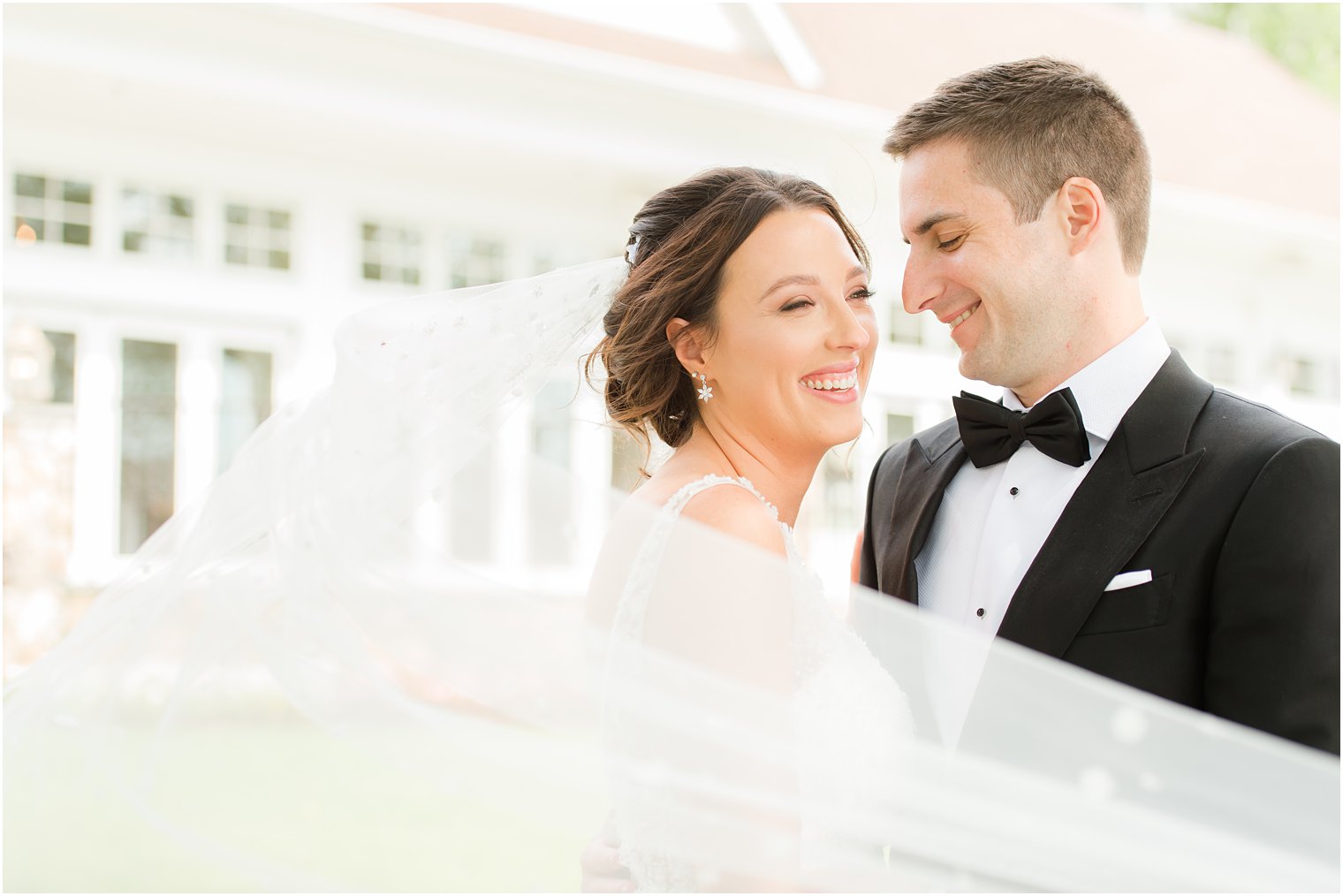 bride and groom laugh together outside Indian Trail Club with bride's veil wrapped around them