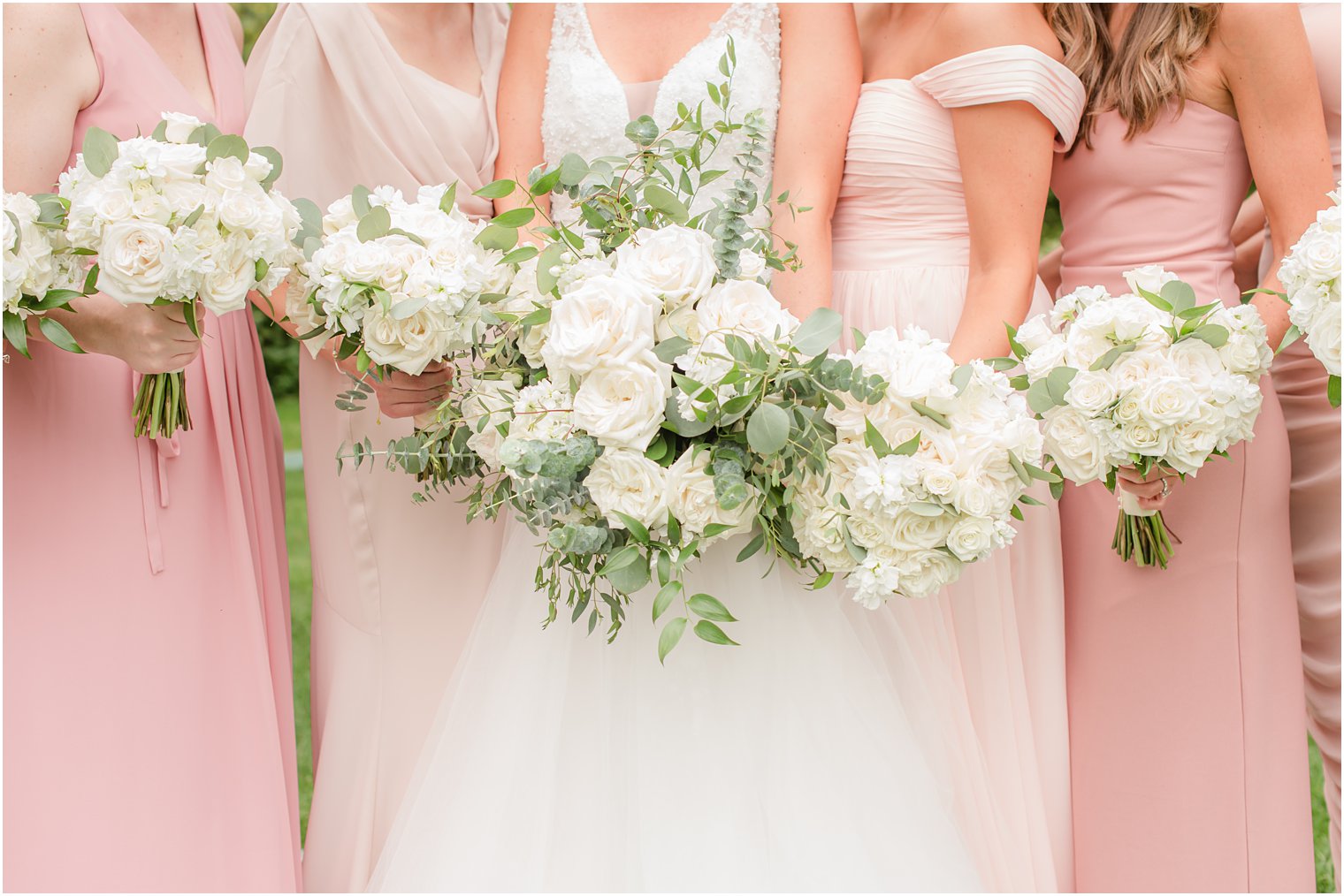 bride and bridesmaids in pink dresses hold ivory floral bouquets