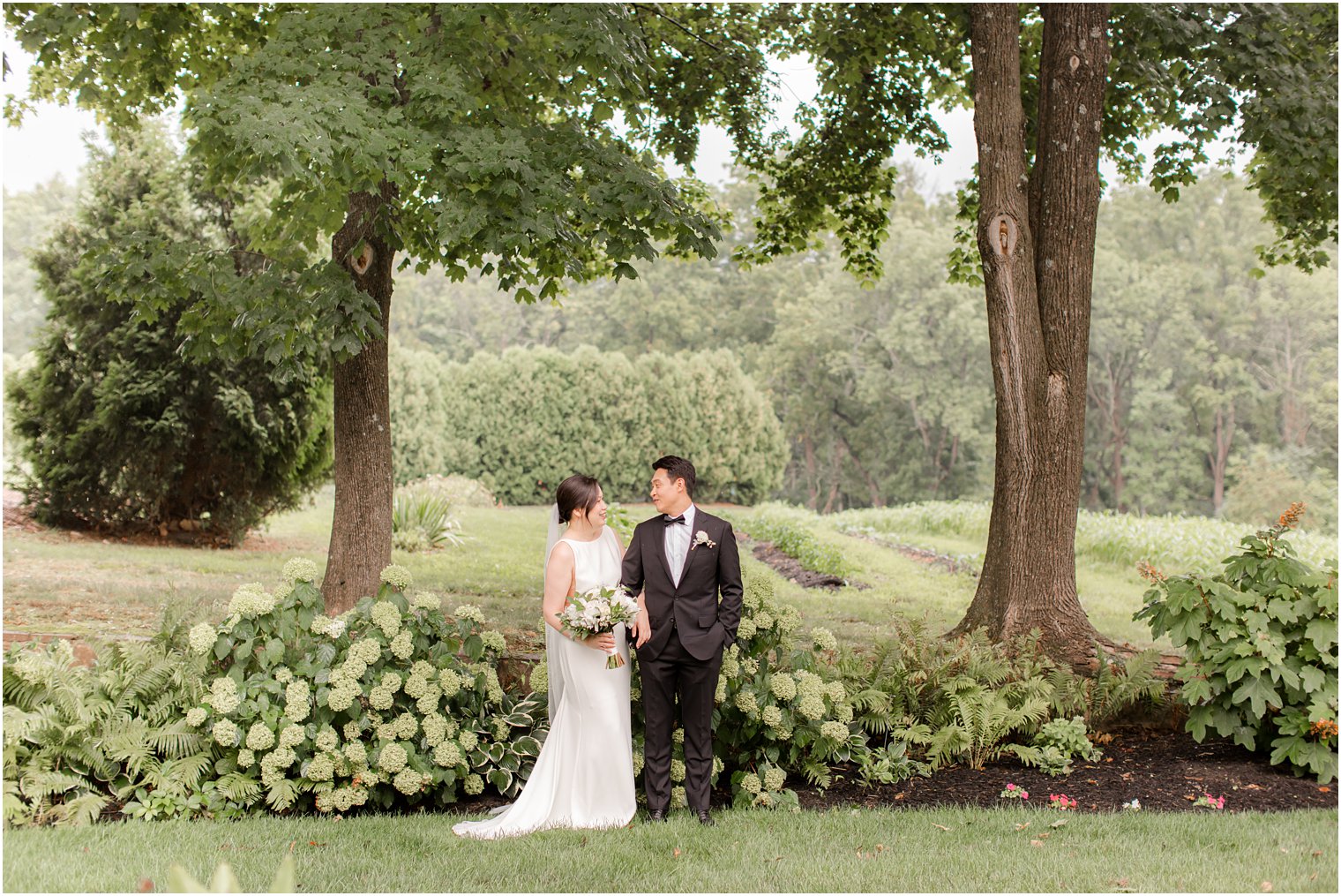bride and groom smile at each other by hydrangea bushes at Ninety Acres