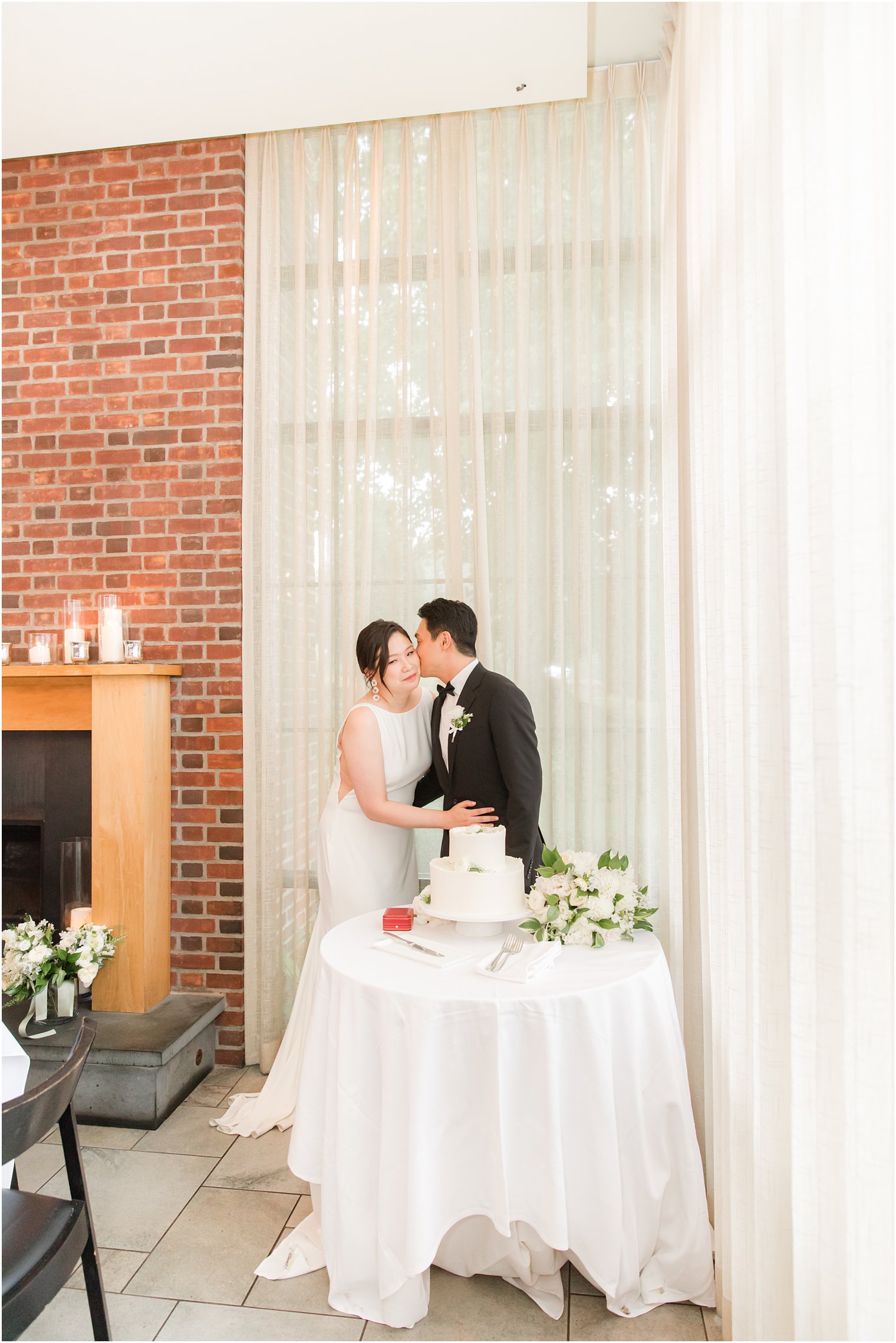 groom kisses bride's cheek before cutting cake