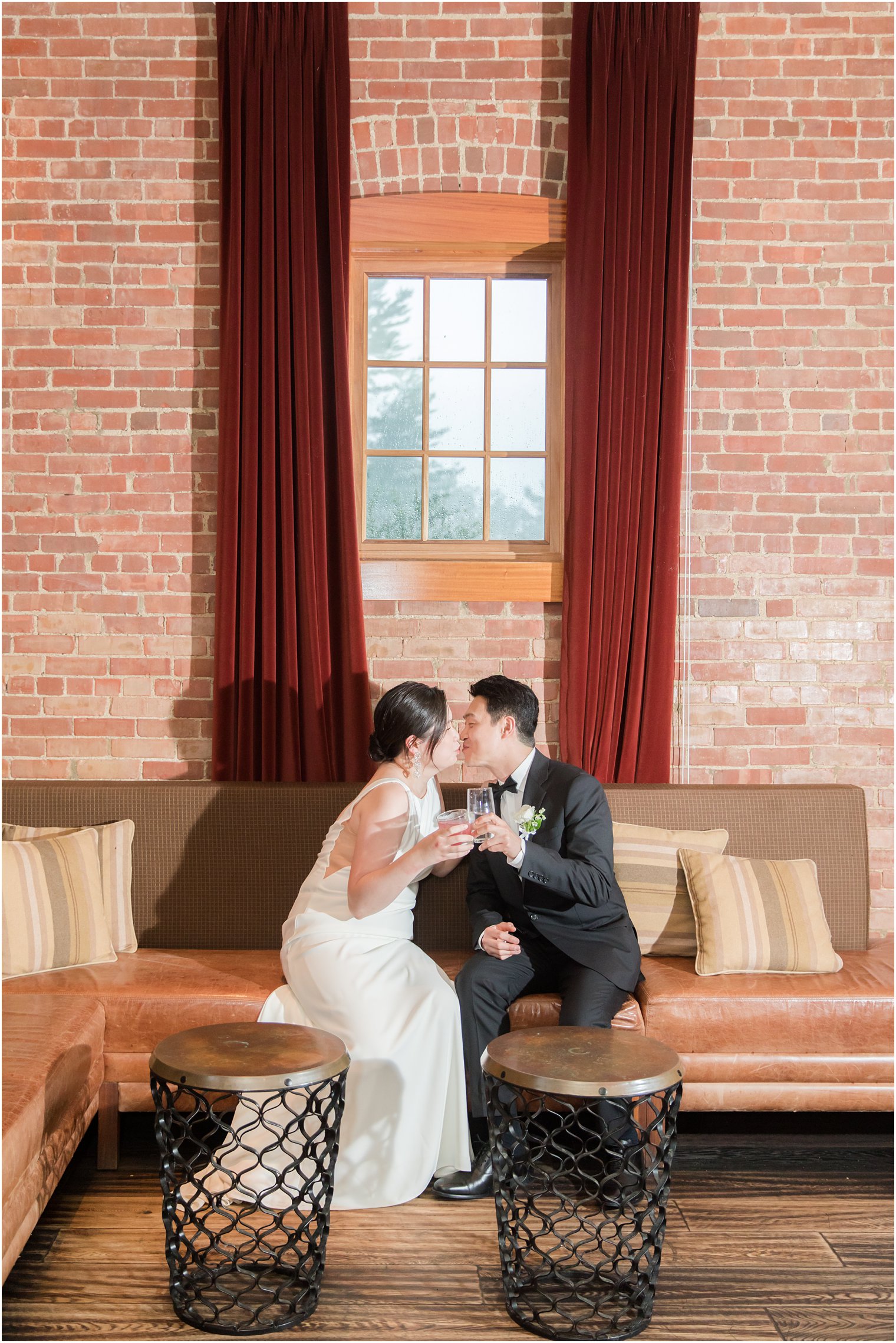 newlyweds kiss holding champagne on couch at Ninety Acres