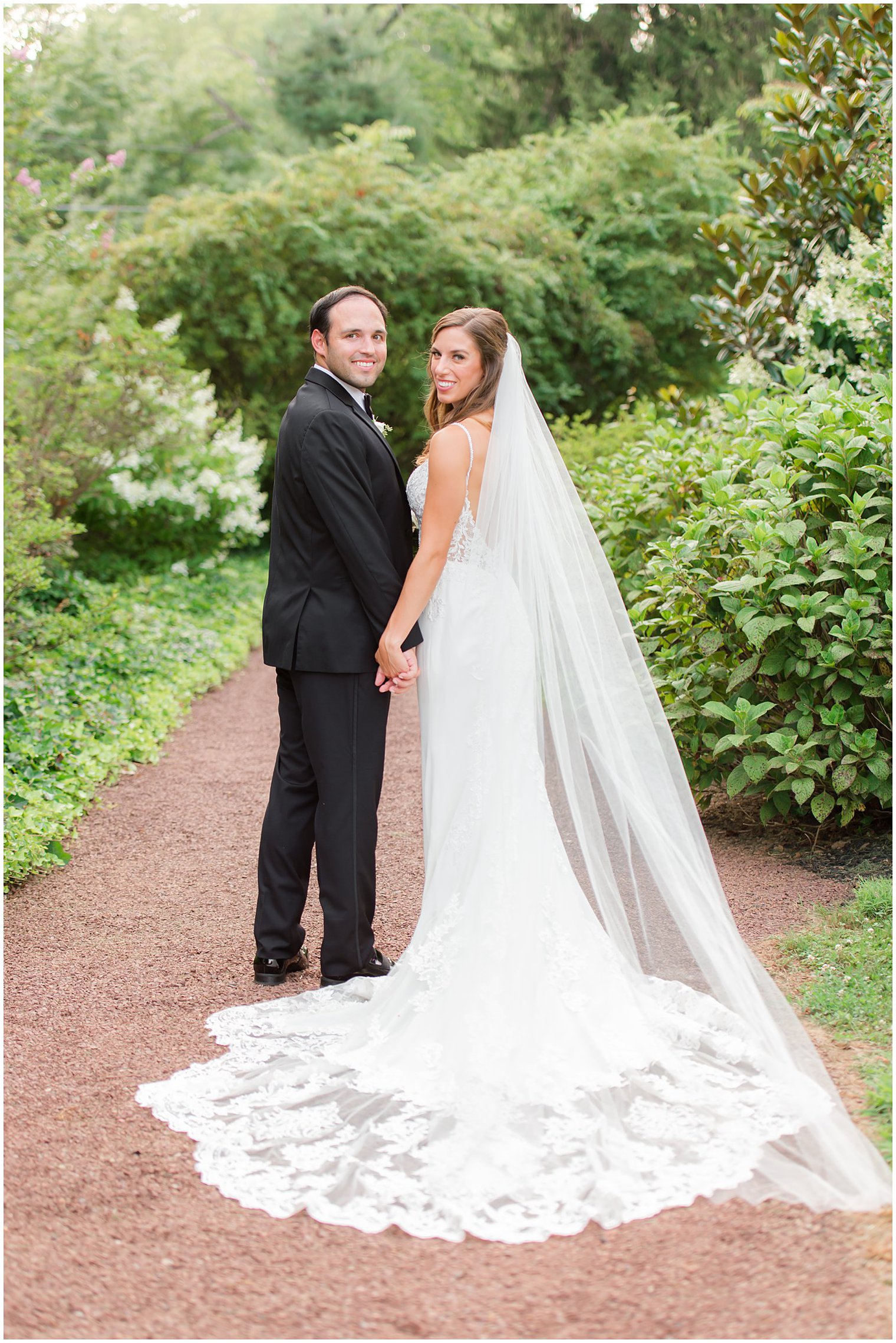 bride and groom hold hands looking over their shoulders during wedding photos at the Inn at Fernbrook Farms