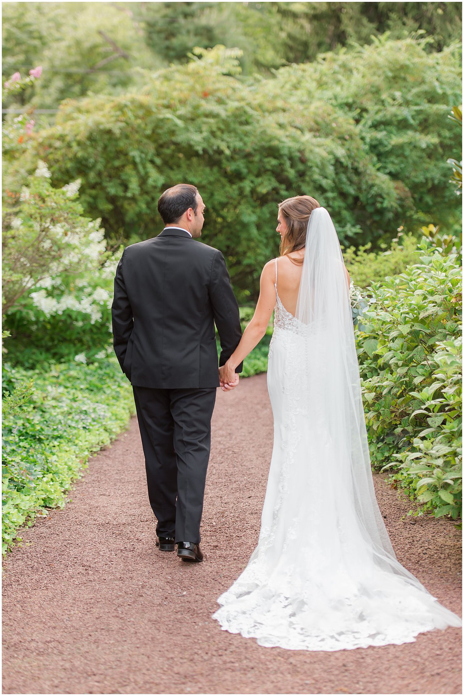 newlyweds hold hands walking through gardens at Inn at Fernbrook Farms