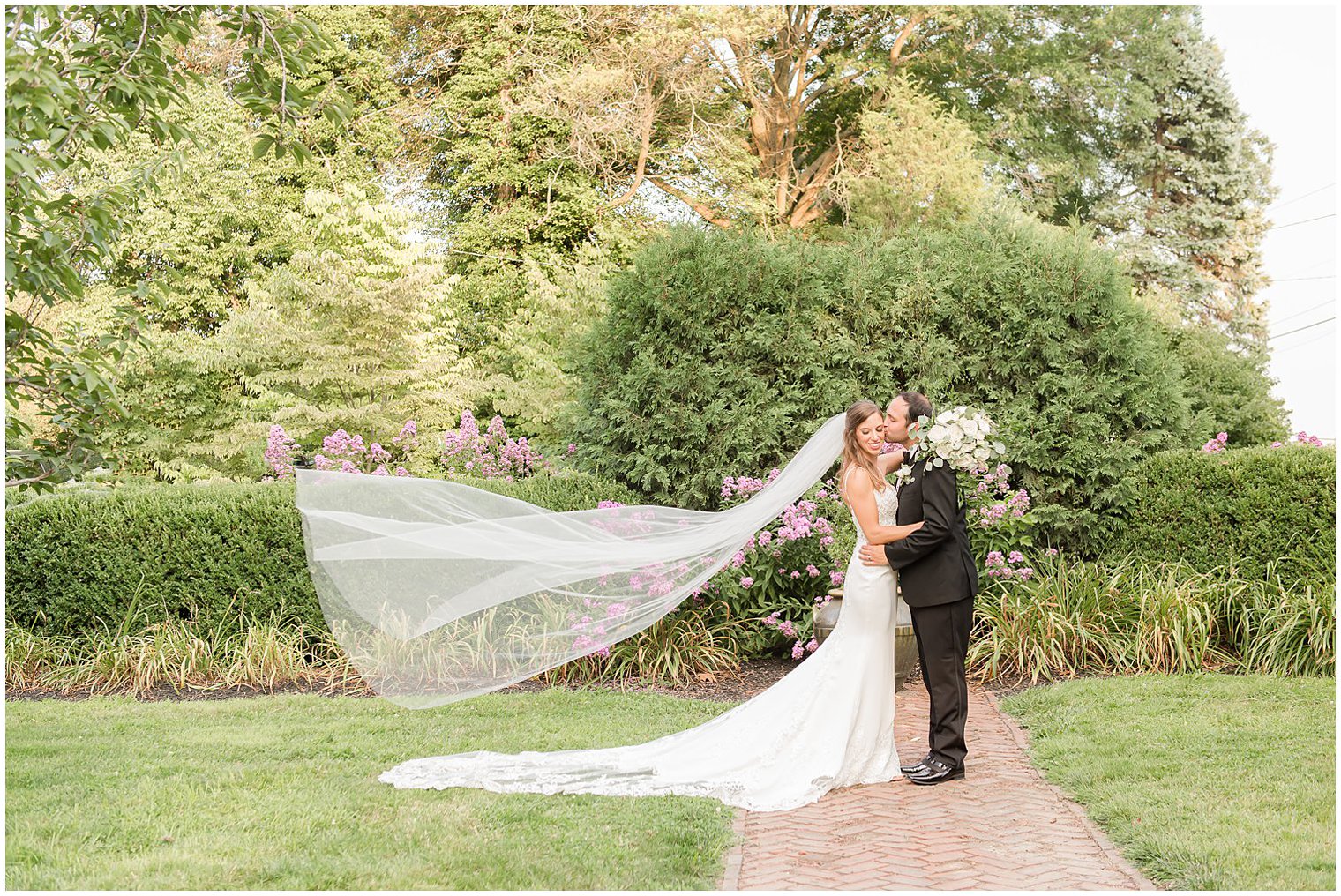 groom kisses bride's cheek while veil floats behind her