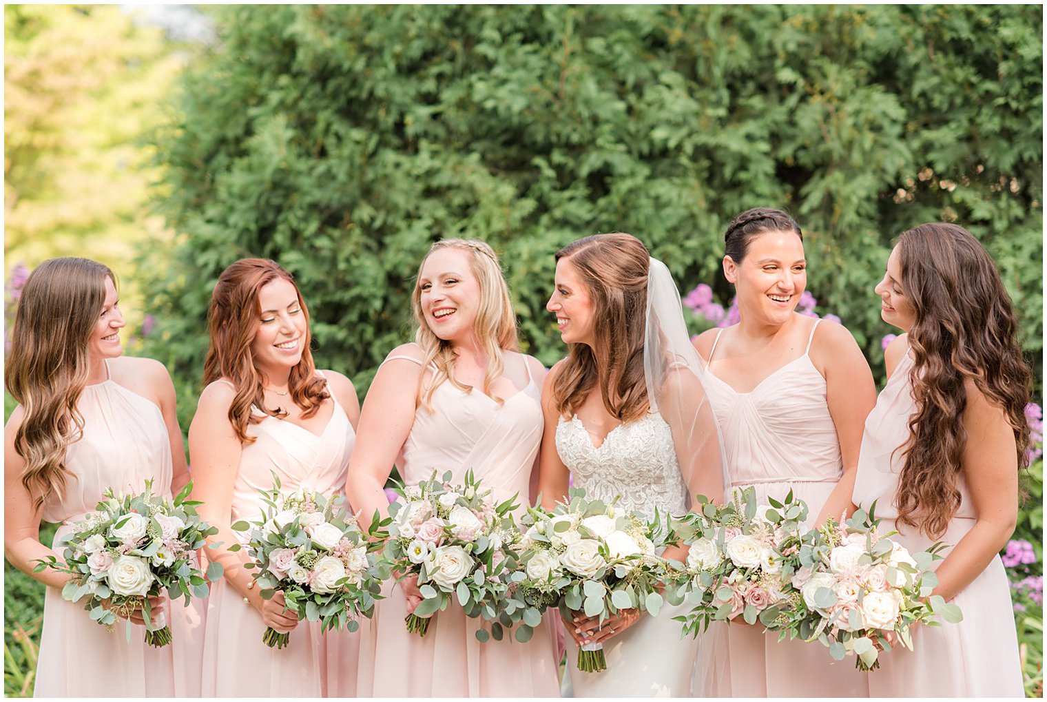 bride laughs with bridesmaids in pastel pink gowns for summer NJ wedding