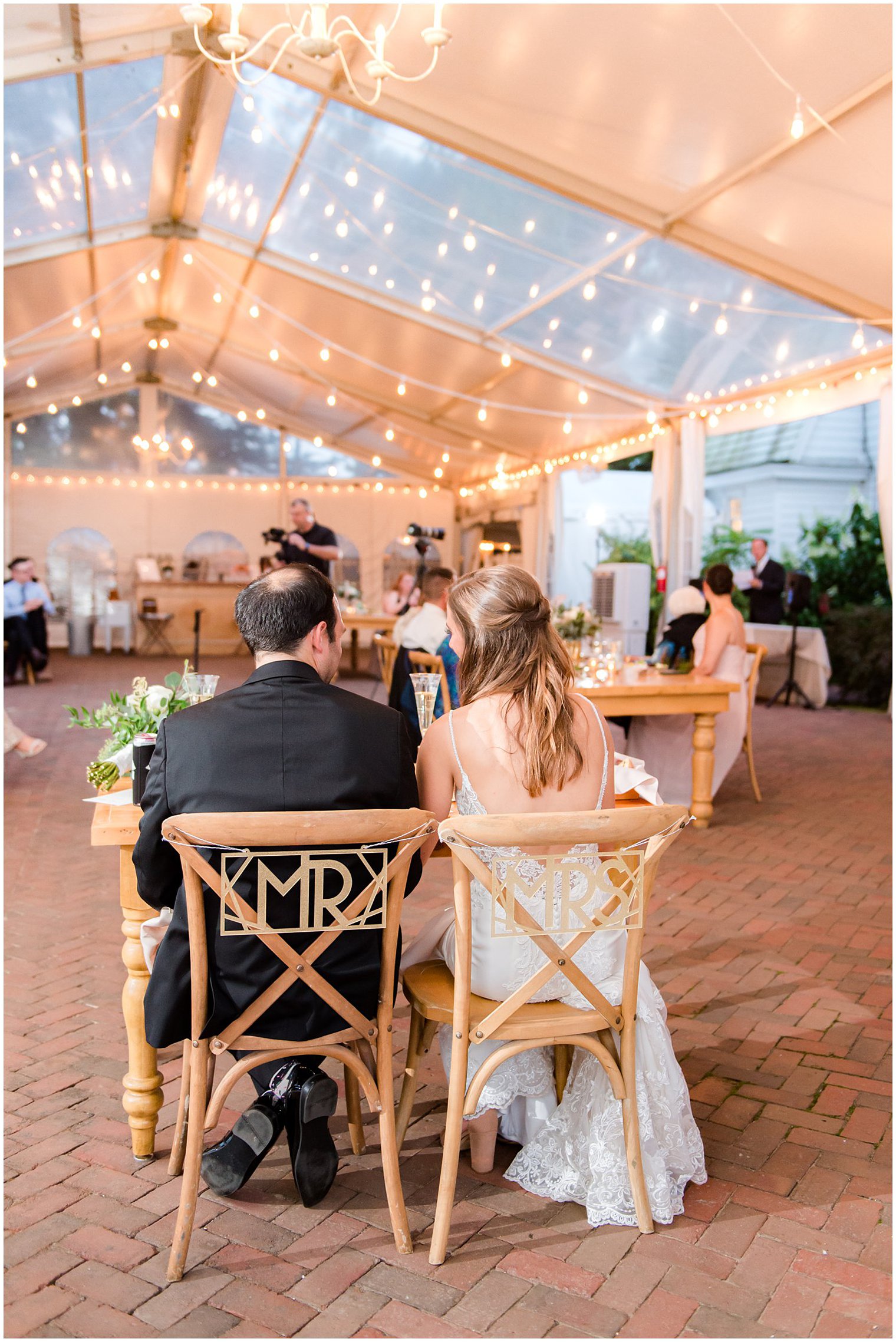 bride and groom sit in wooden chairs with gold Mr and Mrs signs
