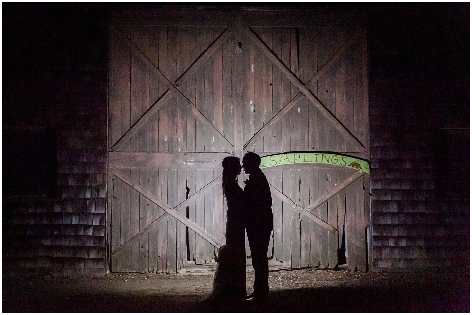 newlyweds pose outside wooden barn door at the Inn at Fernbrook Farms