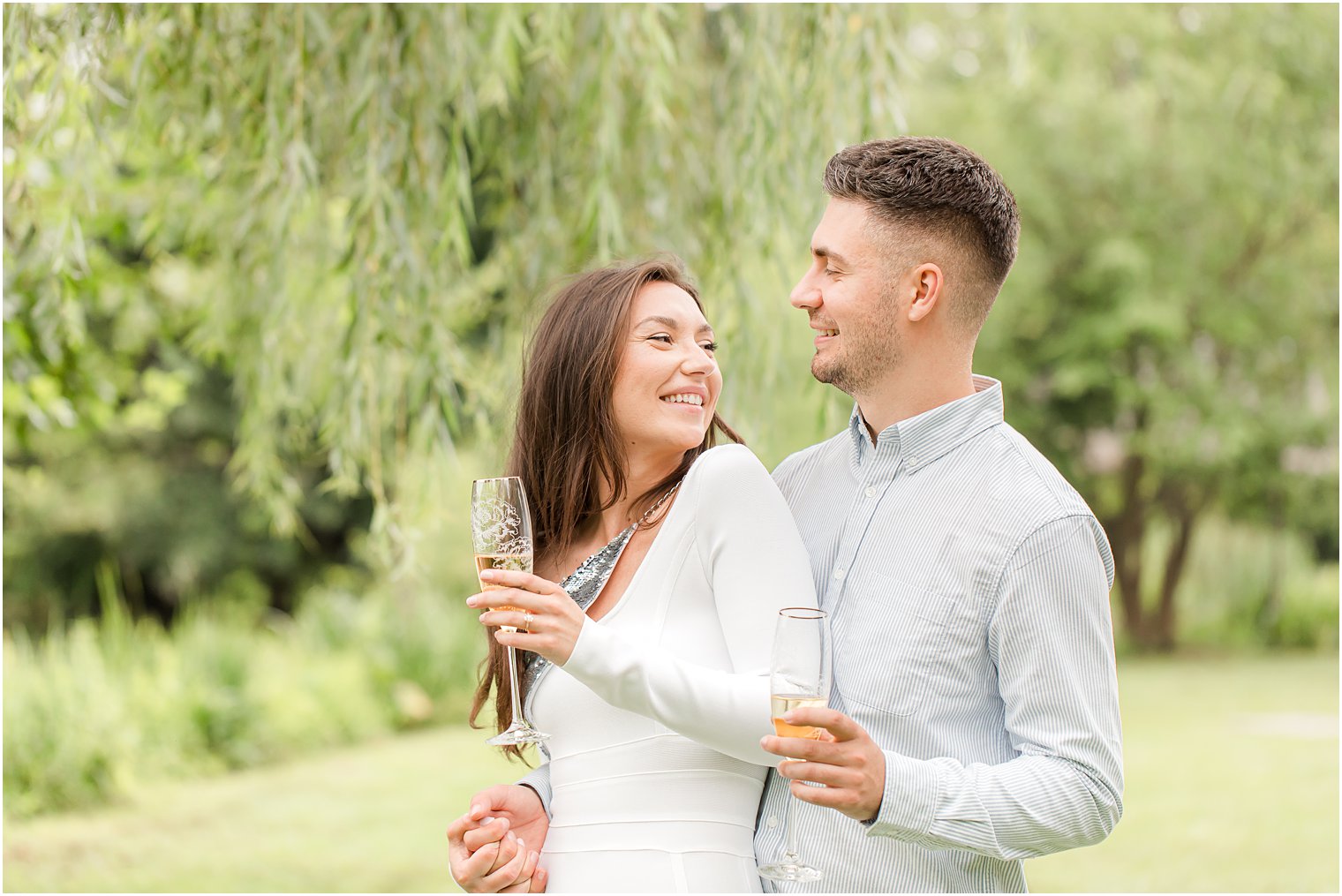 engaged couple holds champagne flutes while hugging 