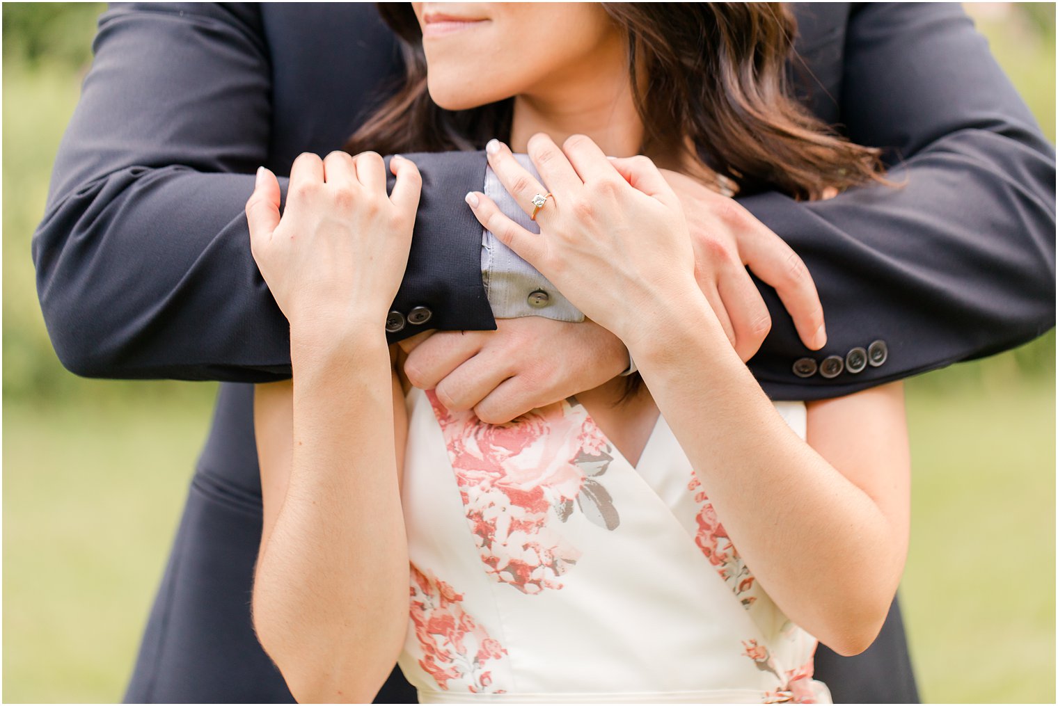 bride holds groom's arms around chest showing off engagement ring 
