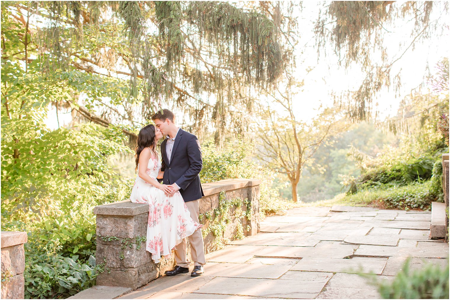 groom kisses bride sitting on stone wall during Skylands Manor engagement session