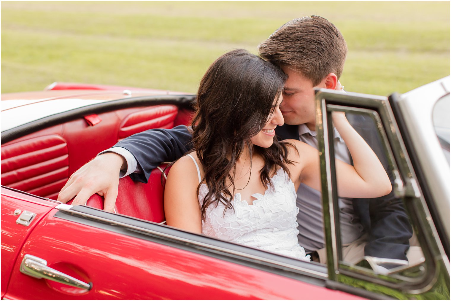 groom nuzzles bride's cheek while sitting in classic red car 