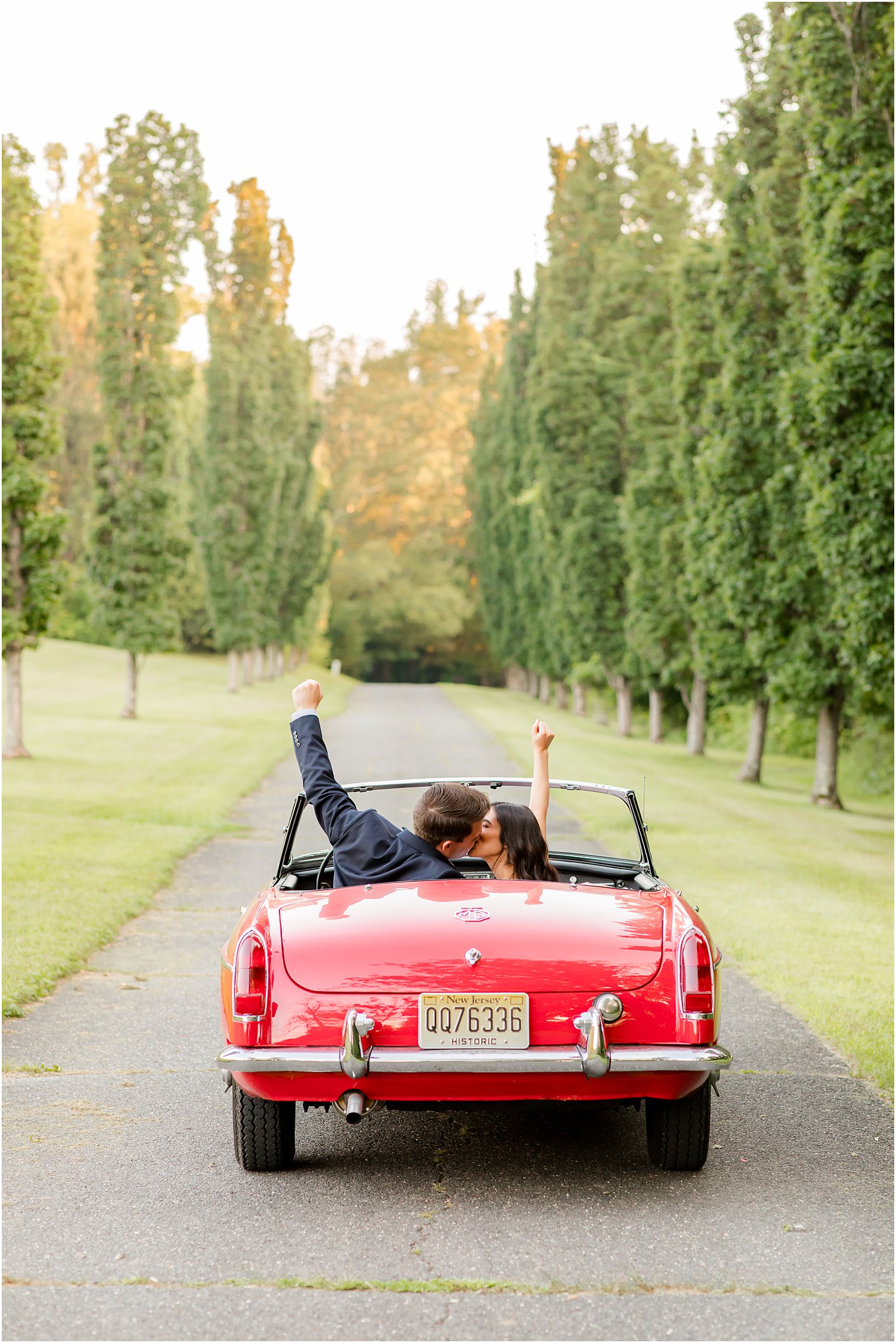 bride and groom raise hands while kissing in red car at Skylands Manor
