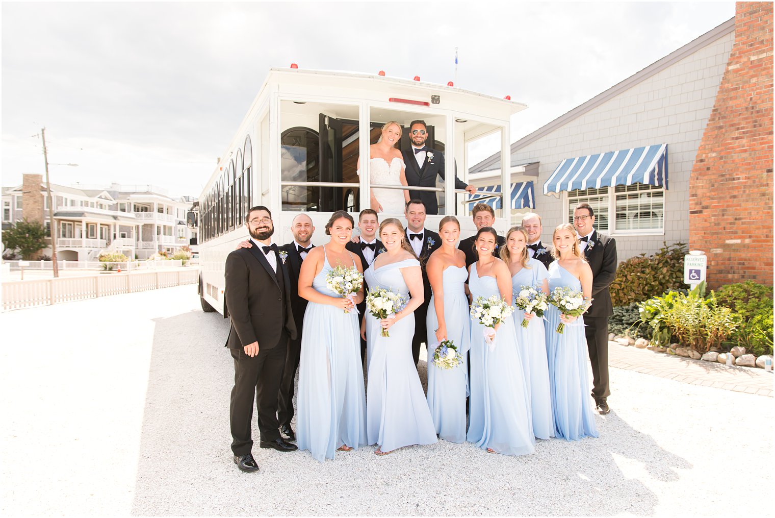 bride and groom pose with wedding party by white trolley at Brant Beach Yacht Club