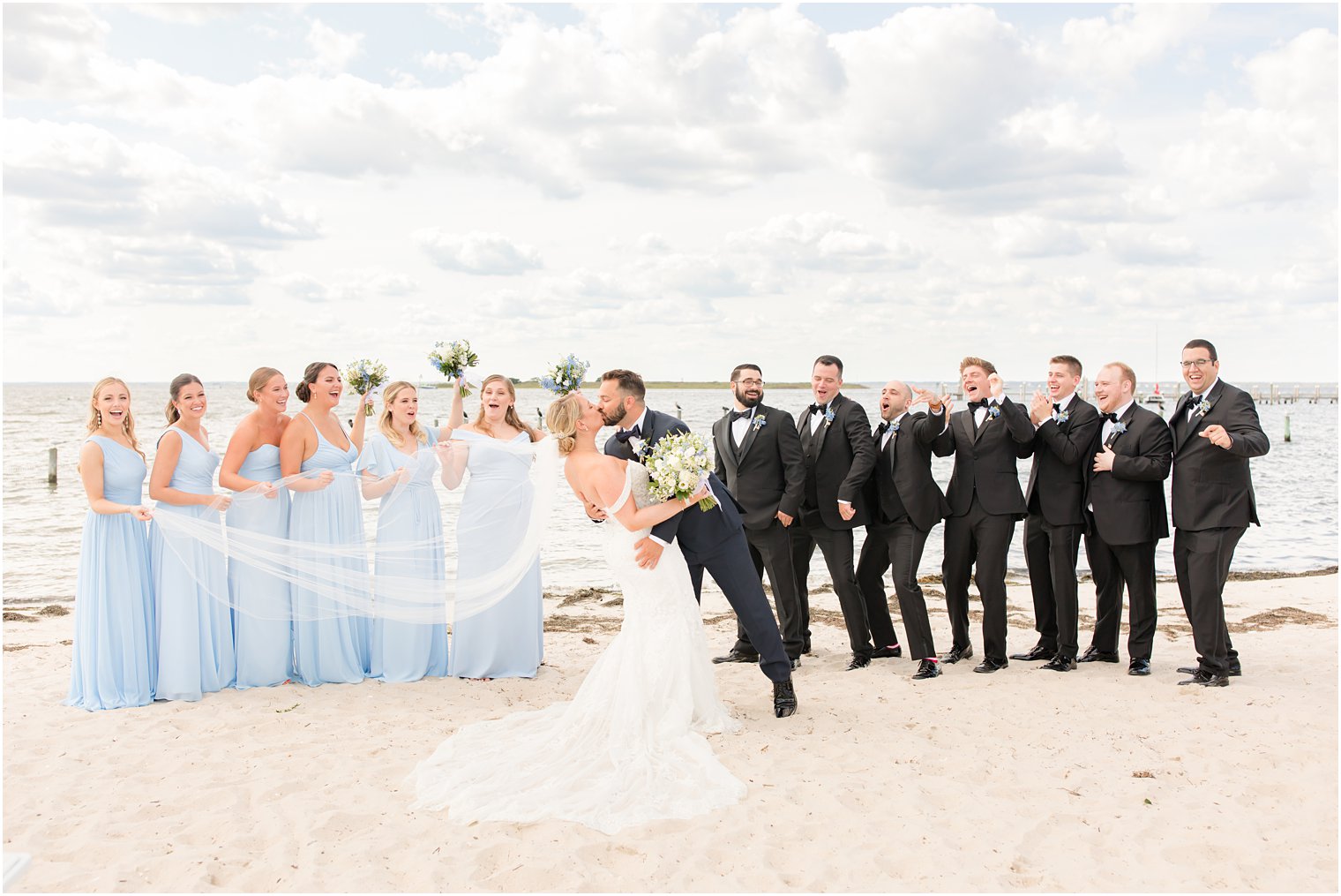 bride and groom kiss while wedding party cheers