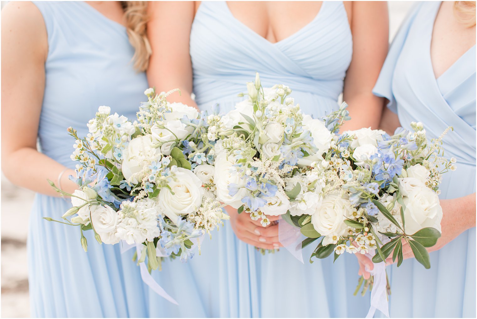 bridesmaids in light blue gowns hold blue and white bouquets