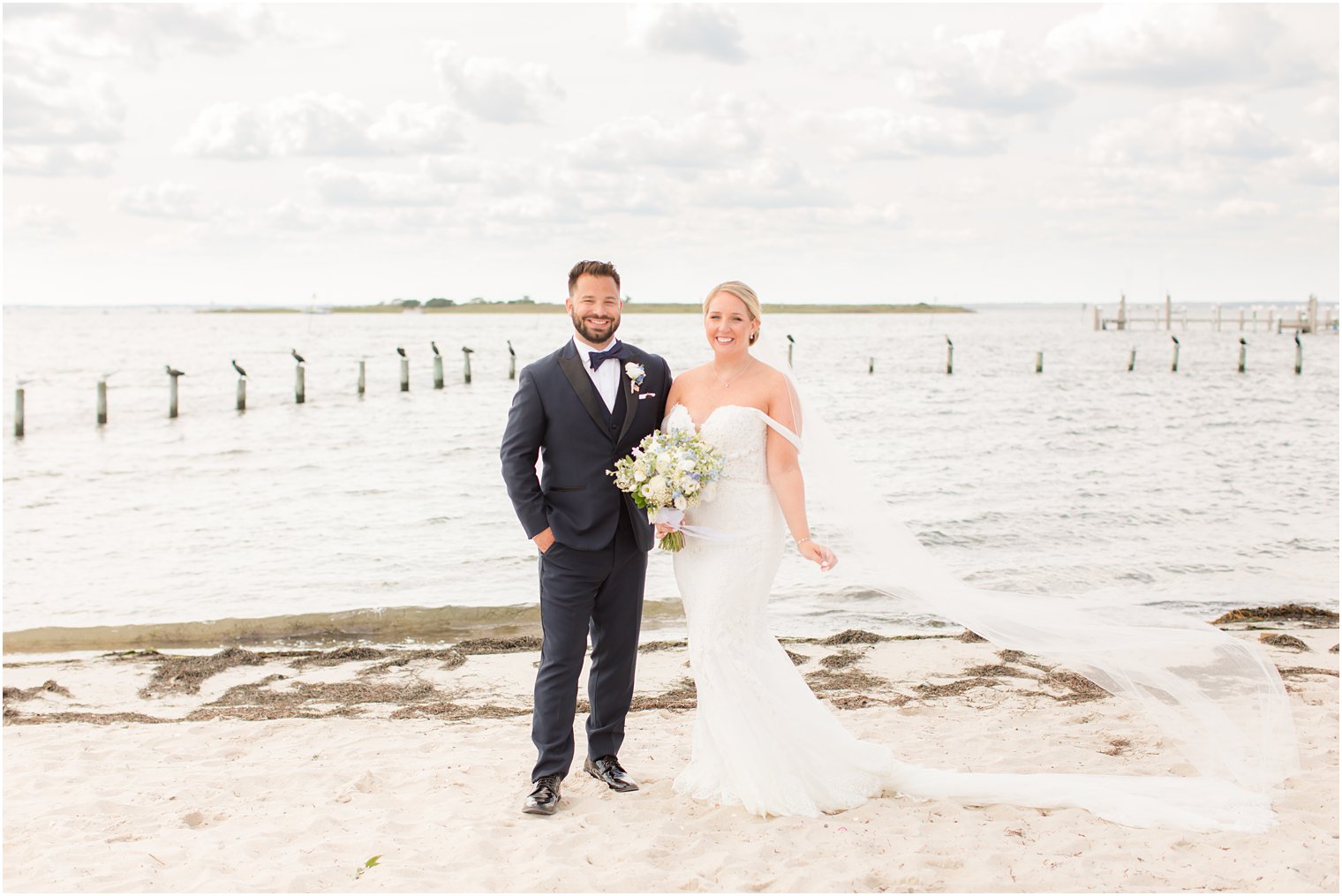 bride holds veil while standing with groom on beach on Long Beach Island