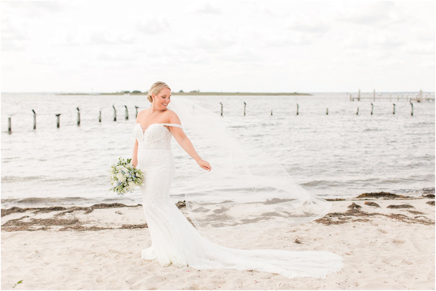 bride holds veil behind her and looks over shoulder at Brant Beach Yacht Club