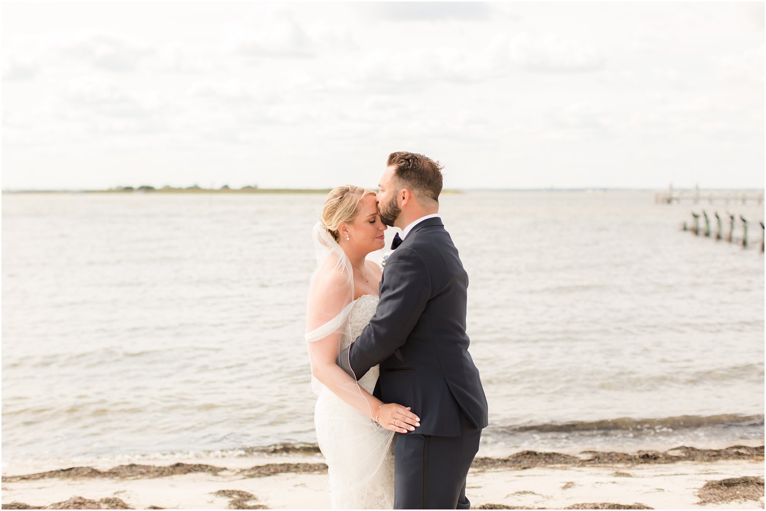 groom hugs bride and kisses her forehead on Long Beach Island