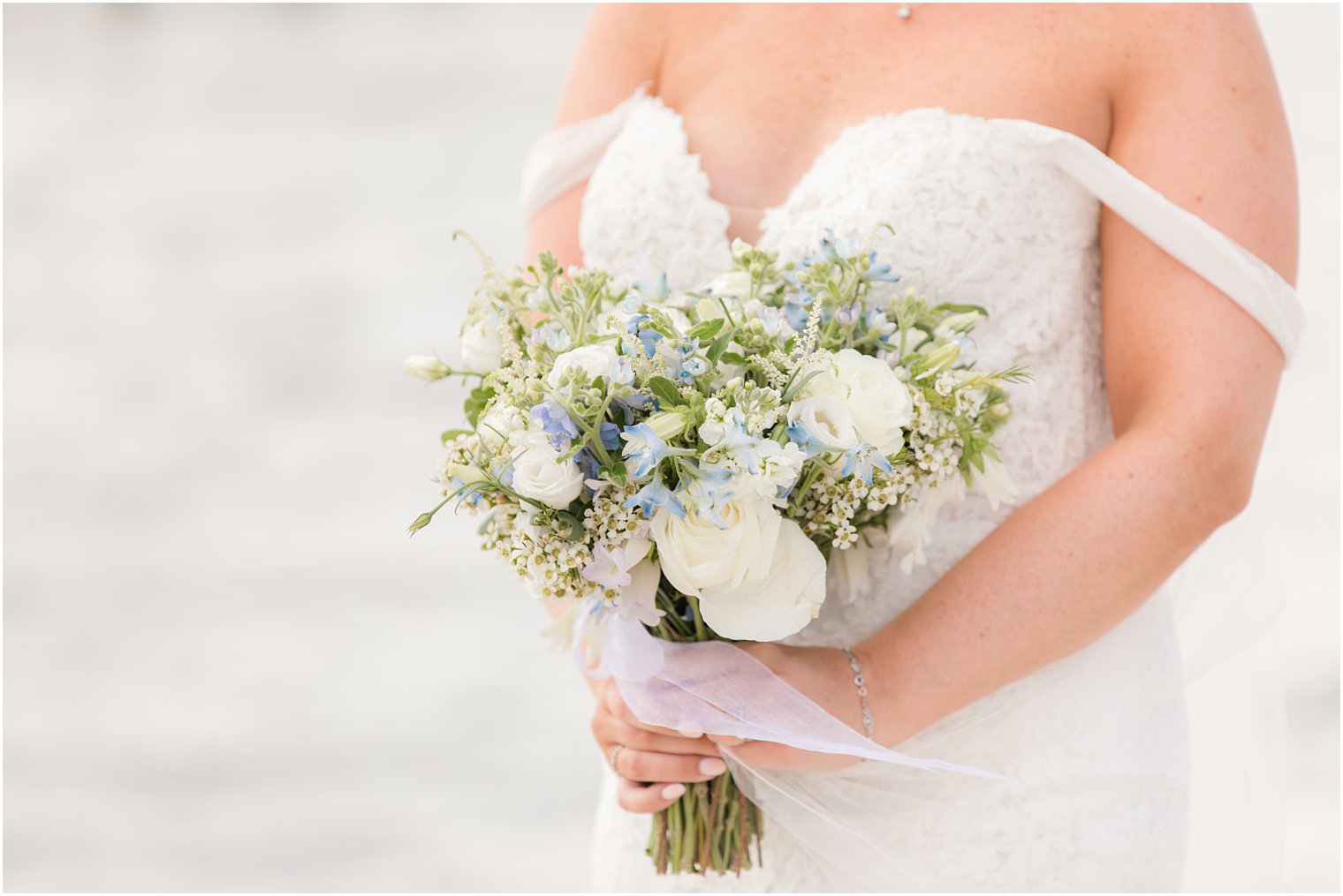 bride holds bouquet of ivory and blue flowers on NJ beach