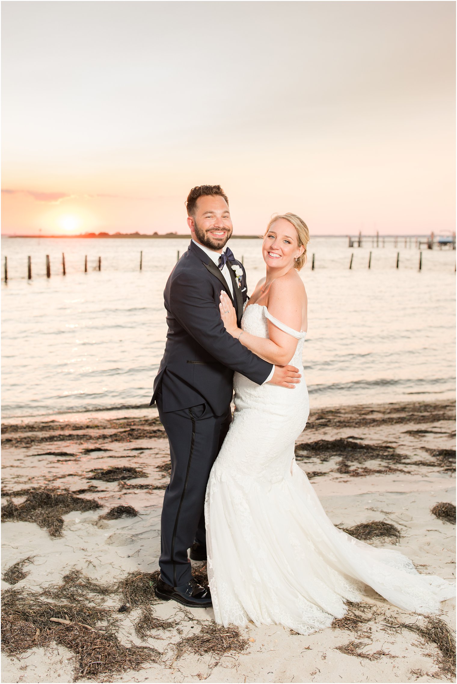 bride and groom pose on beach at sunset on wedding day