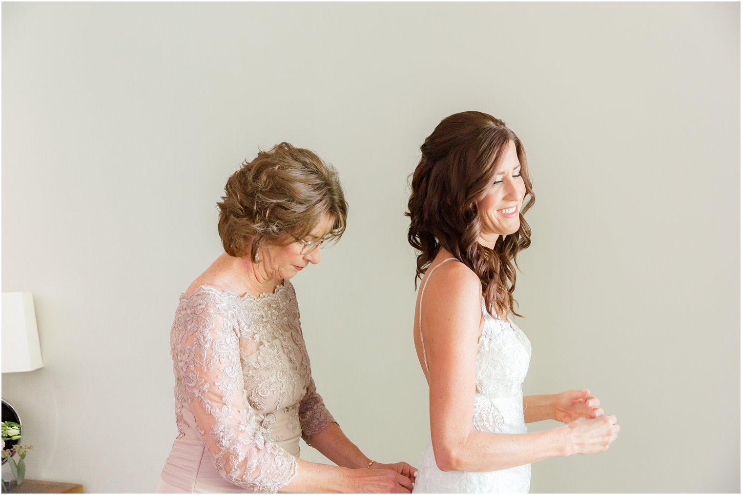 mother helps bride button wedding dress on morning of wedding 