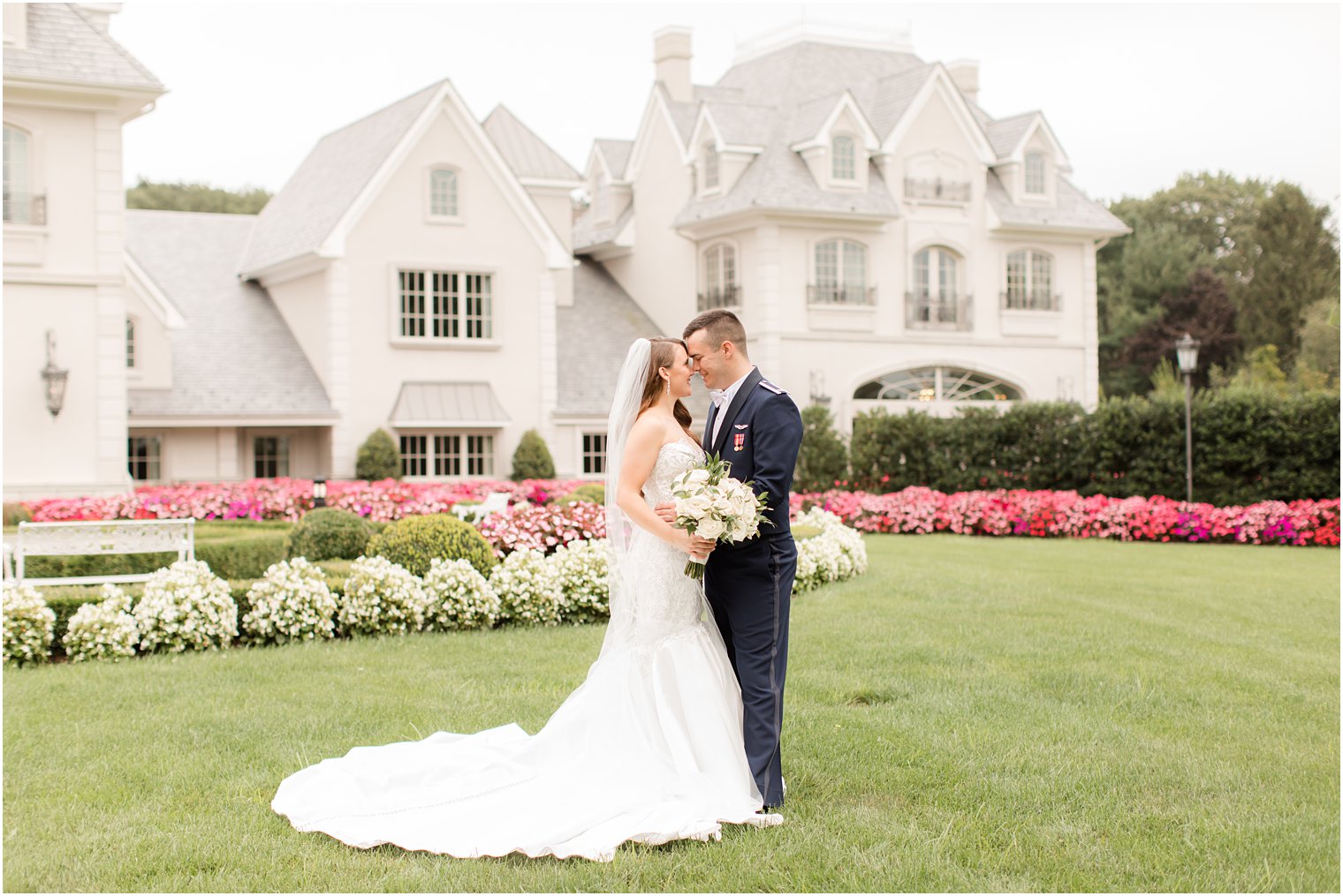 bride and groom pose on lawn with pink and ivory flowers at Park Chateau Estate