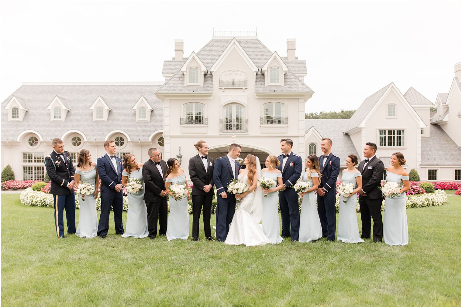 newlyweds look at each other with wedding party beside them on lawn