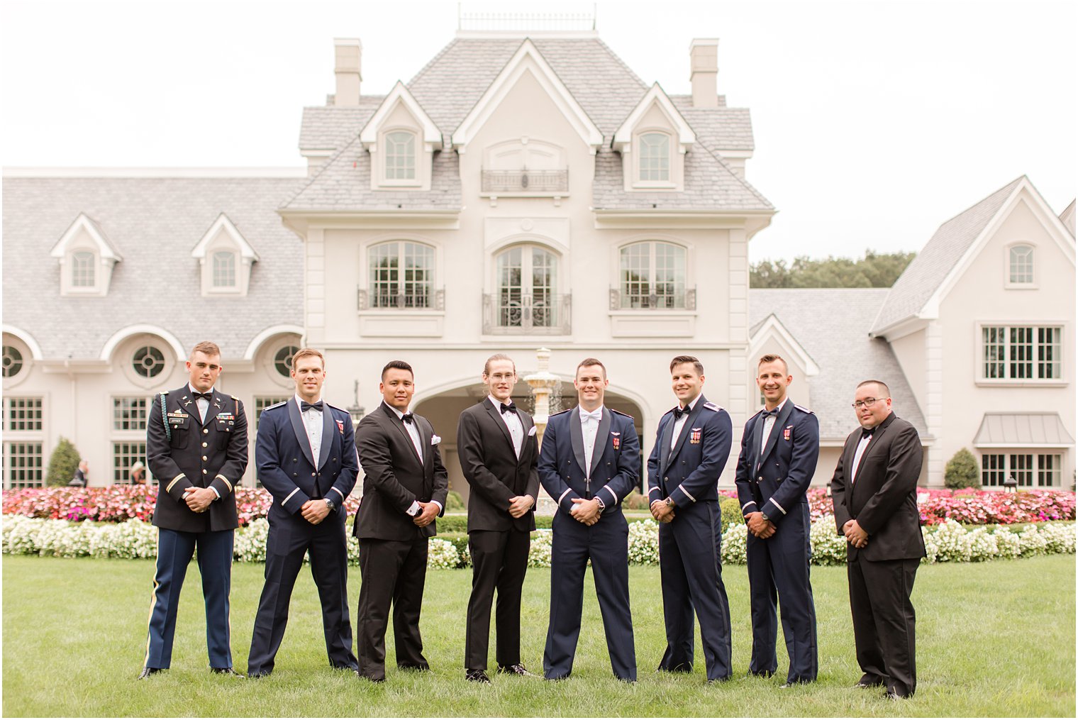 groom poses with groomsmen in black tuxes and military attire 