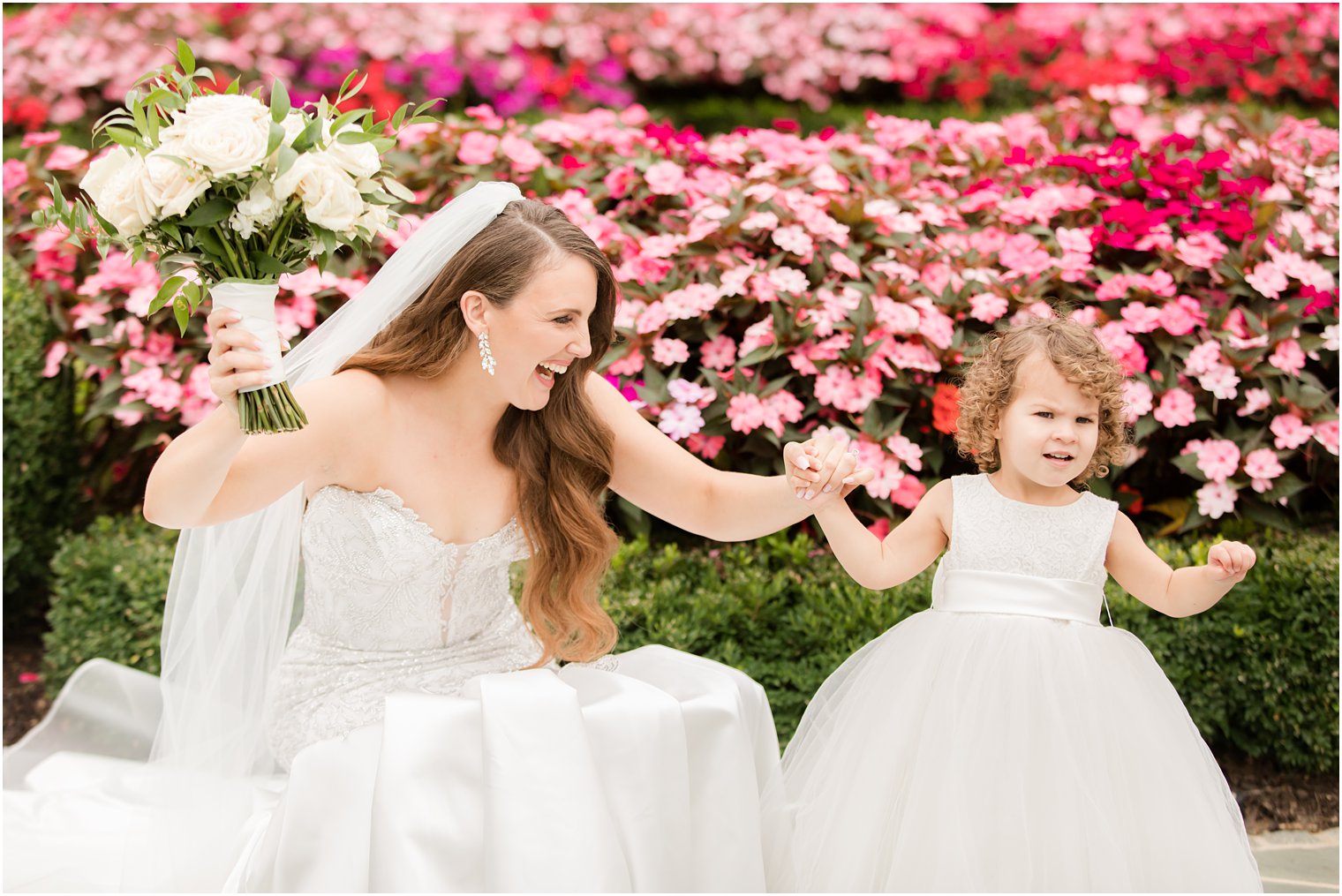 bride dances with flower girl by pink flowers 
