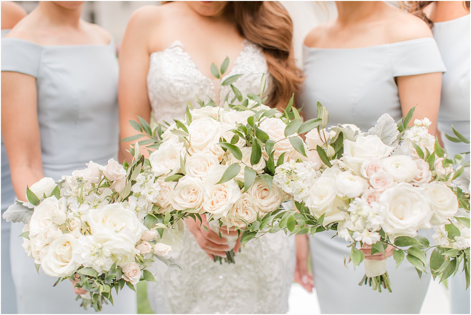 bride and bridesmaids hold bouquets with ivory and pastel flowers 