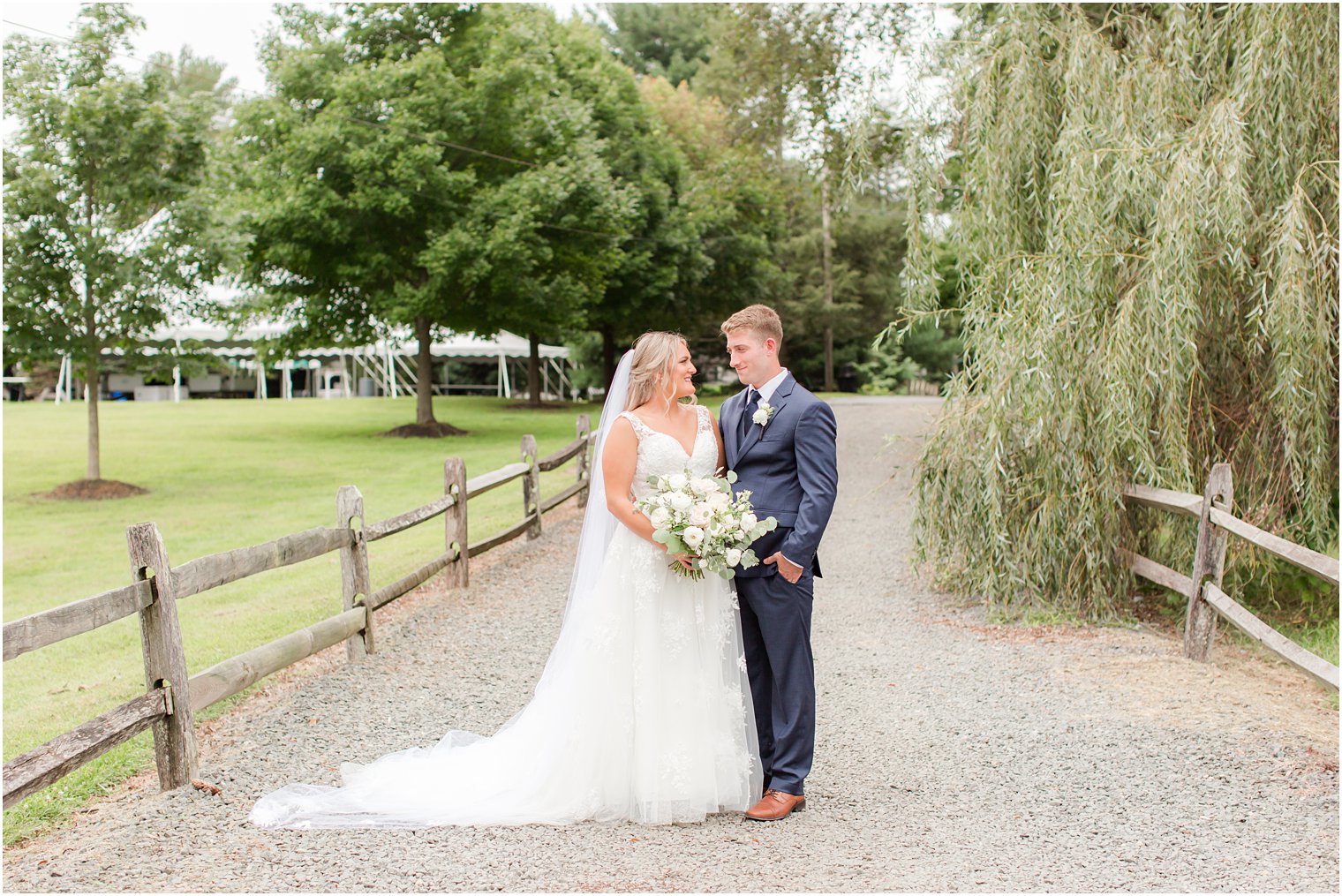 bride and groom smile at each other on pathway at Windows on the Water at Frogbridge