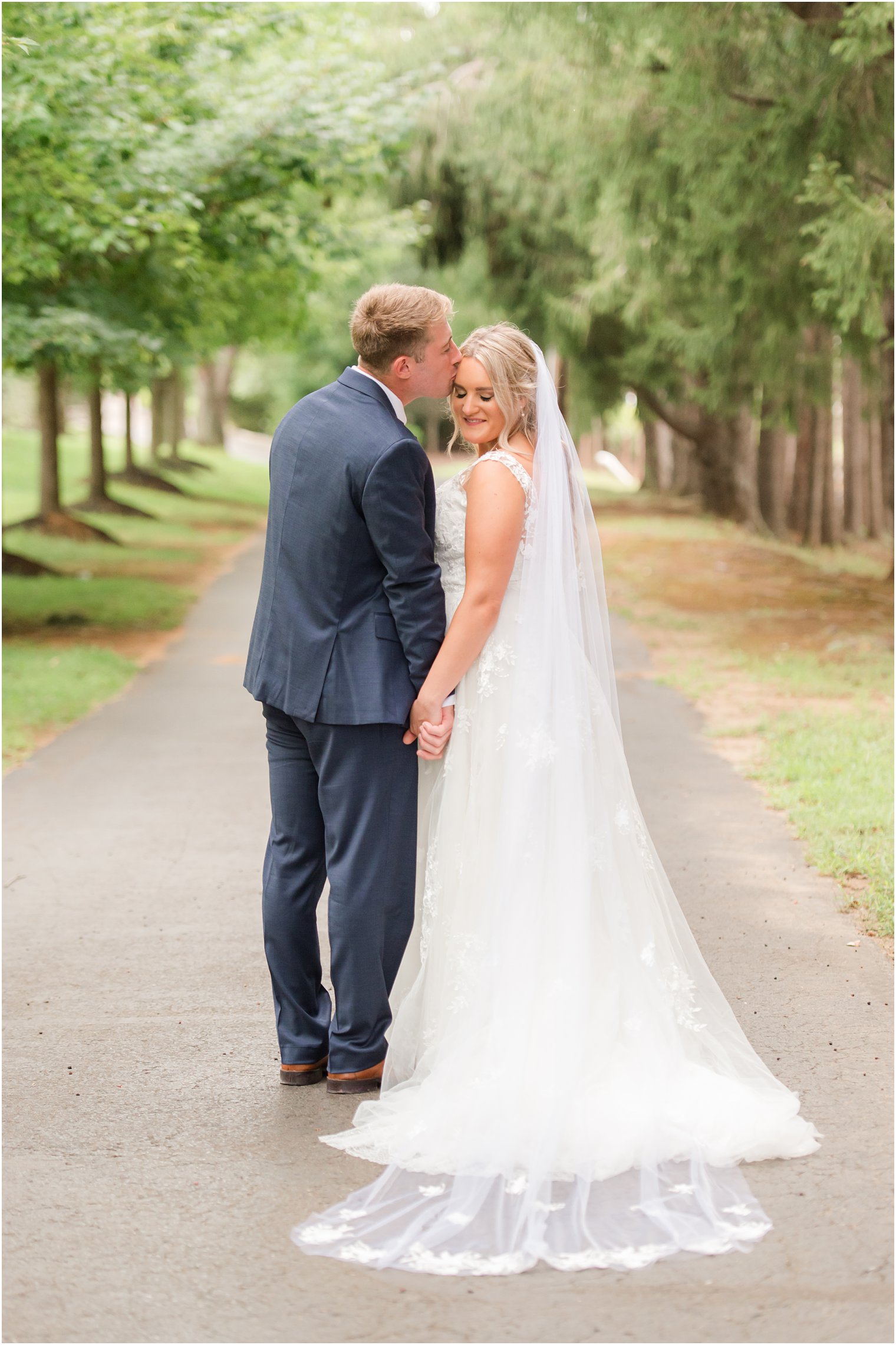 bride and groom hold hands while groom kisses her forehead 