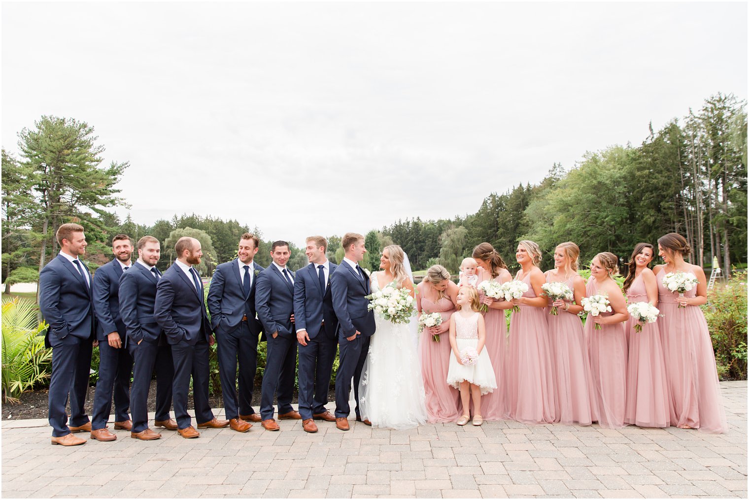 bride and groom smile at each other with wedding party around them 