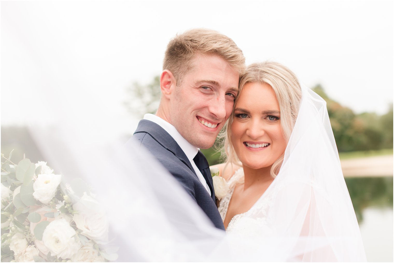 newlyweds lean heads together with veil wrapped around them