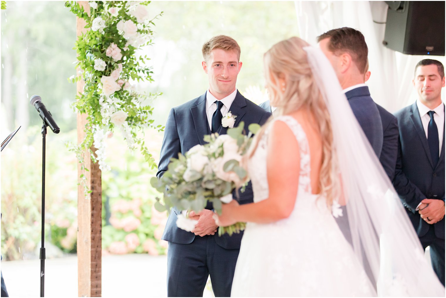 groom looks at bride during wedding ceremony at Windows on the Water at Frogbridge