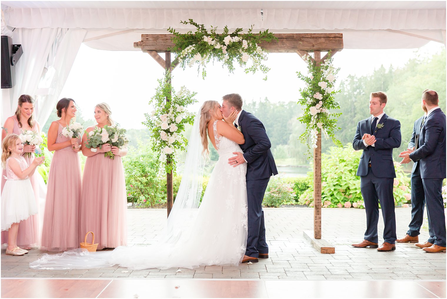 newlyweds kiss during NJ wedding ceremony under wooden arbor