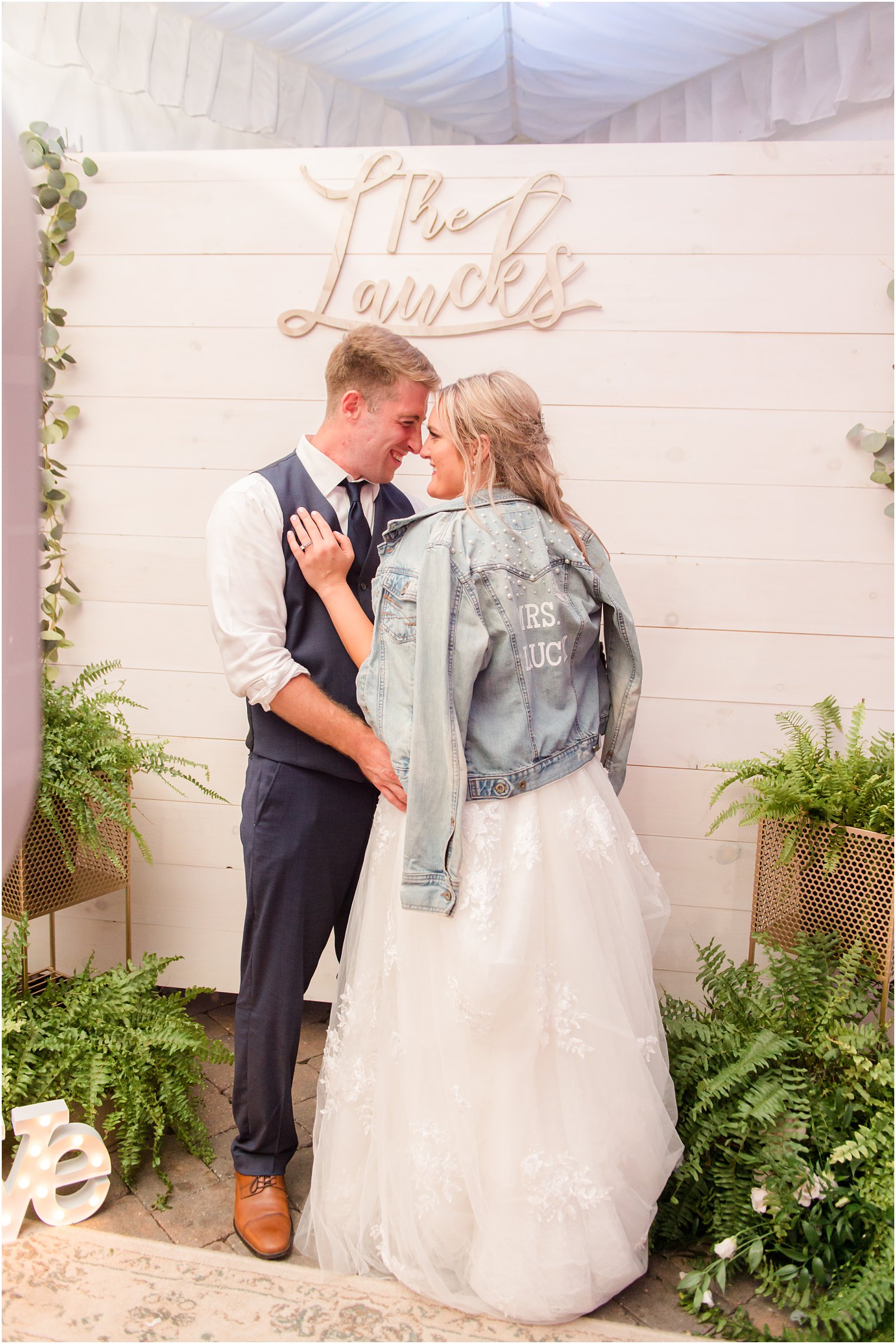 bride and groom pose by wooden wall with name
