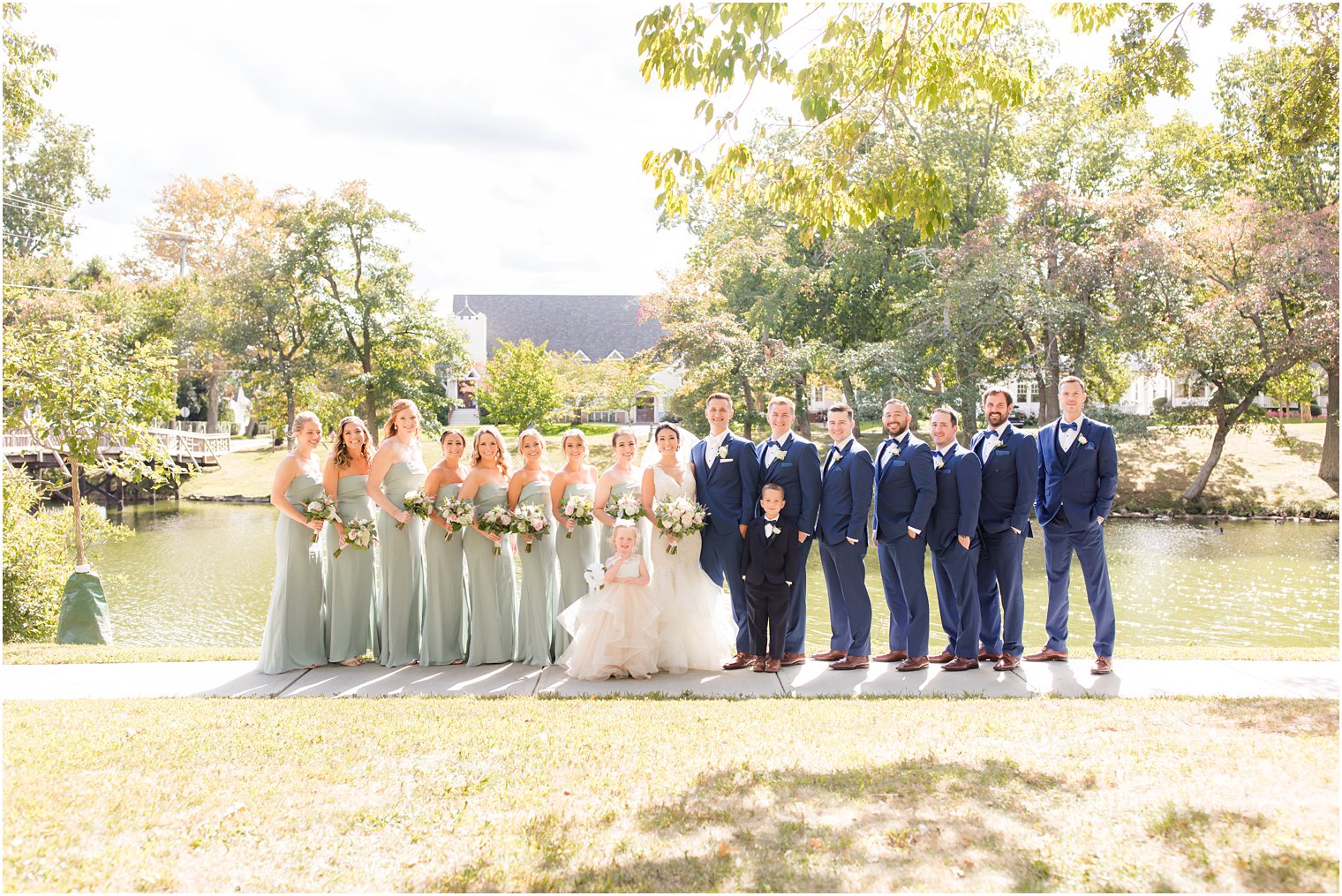 bride and groom stand with wedding party in sage green and navy blue