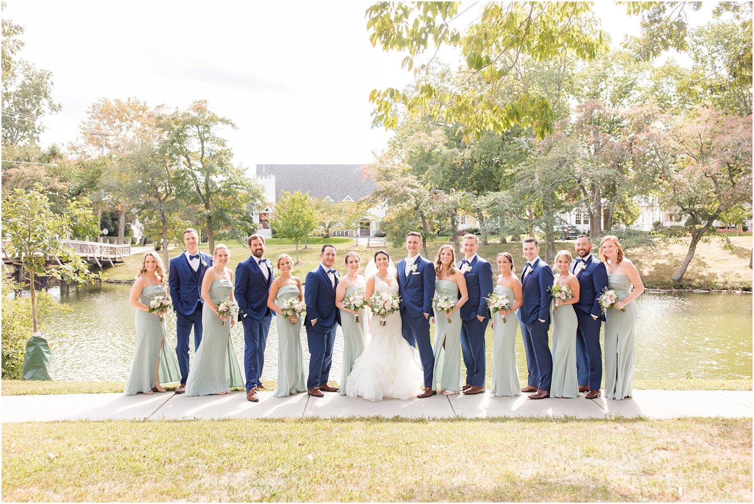 newlyweds pose with wedding party in sage green and navy attire