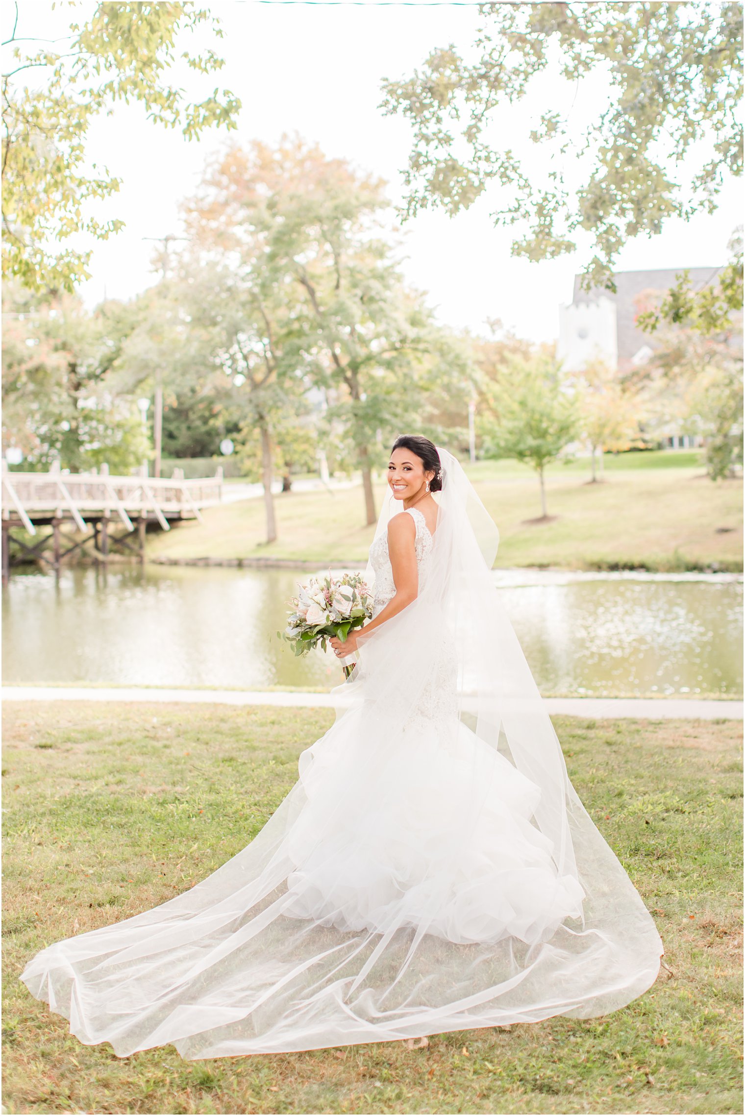 bride poses with veil behind her looking over shoulder in park