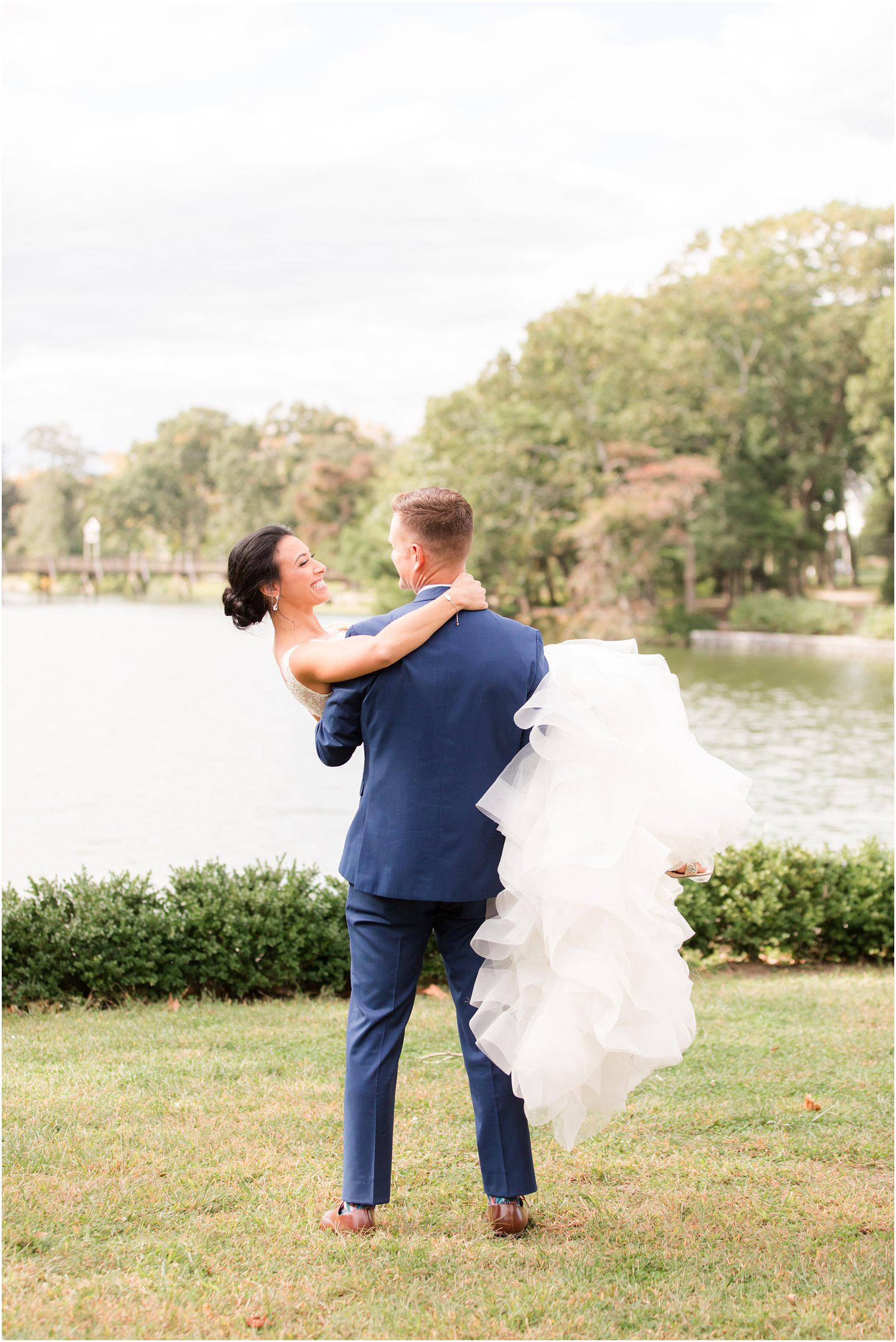 groom lifts bride during NJ wedding portraits by lake