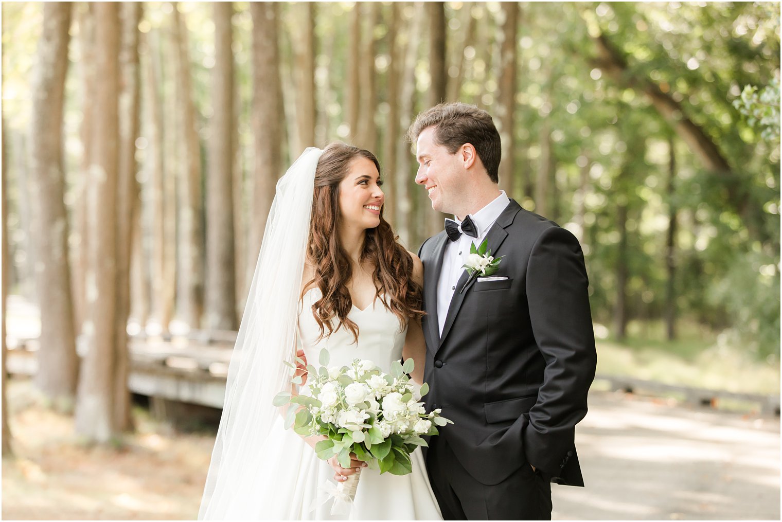 newlyweds smile at each other on wooden pathway at Eagle Oaks