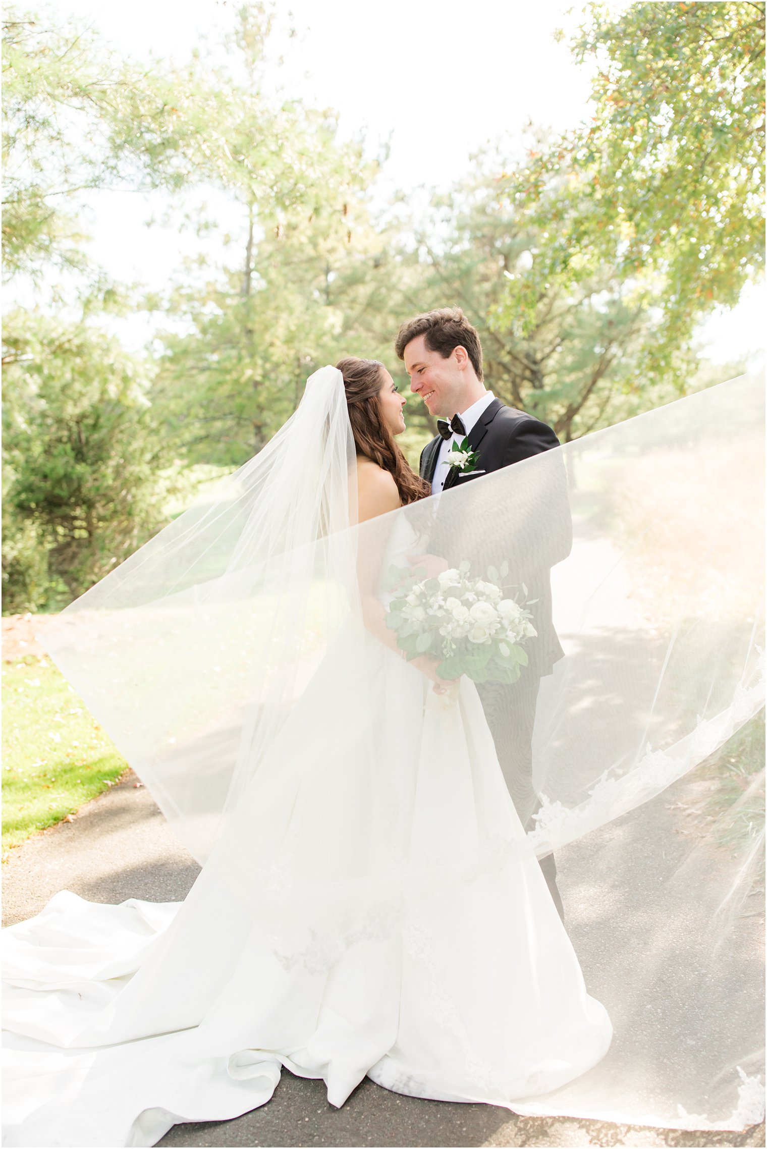 bride and groom smile at each other with veil floating