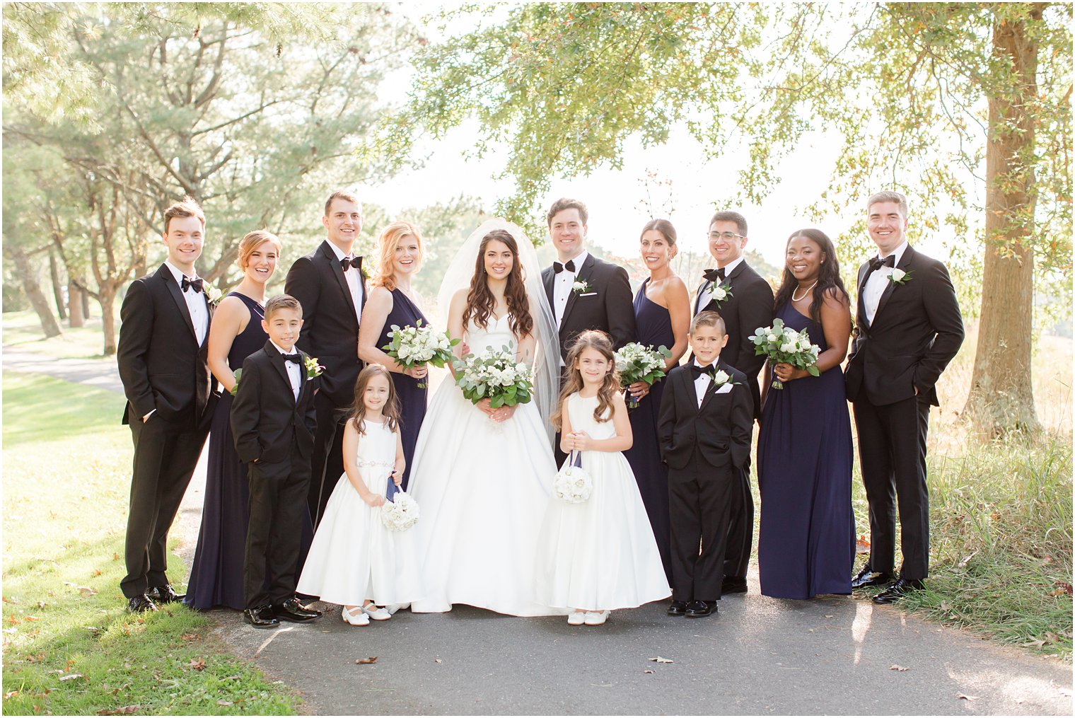 newlyweds pose with wedding party in navy dresses and black tuxes