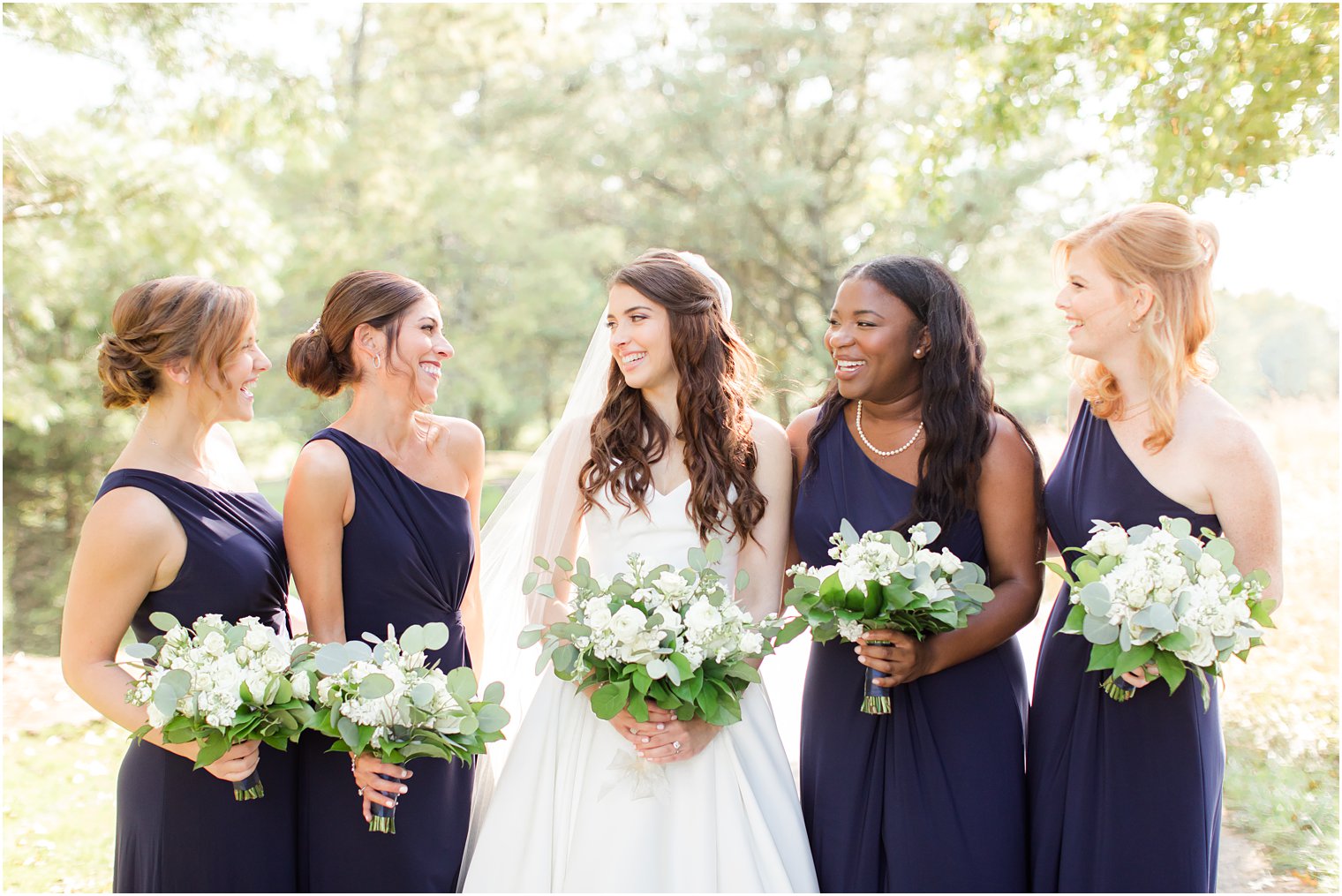 bride poses with bridesmaids in one shoulder navy gowns at Eagle Oaks Golf and Country Club