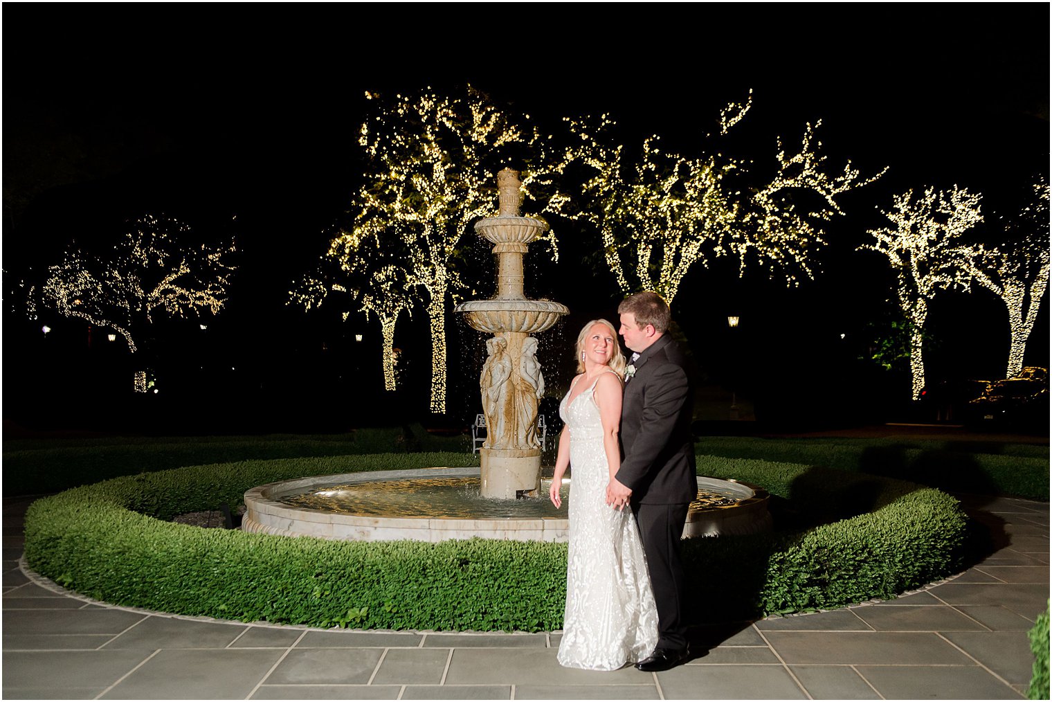 newlyweds in front of lighted trees 